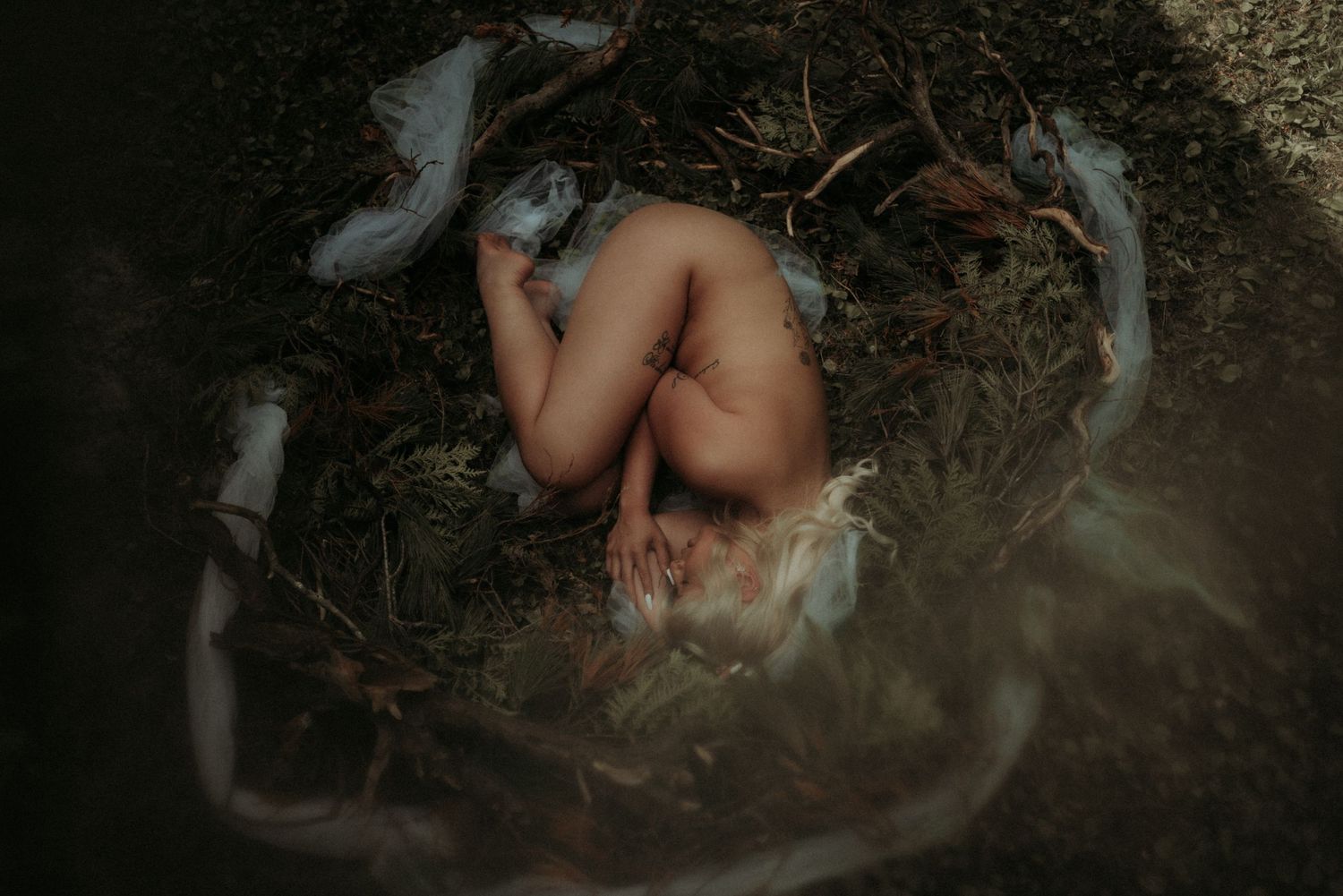 Dramatic outdoor portrait among fallen branches in dark moody setting.