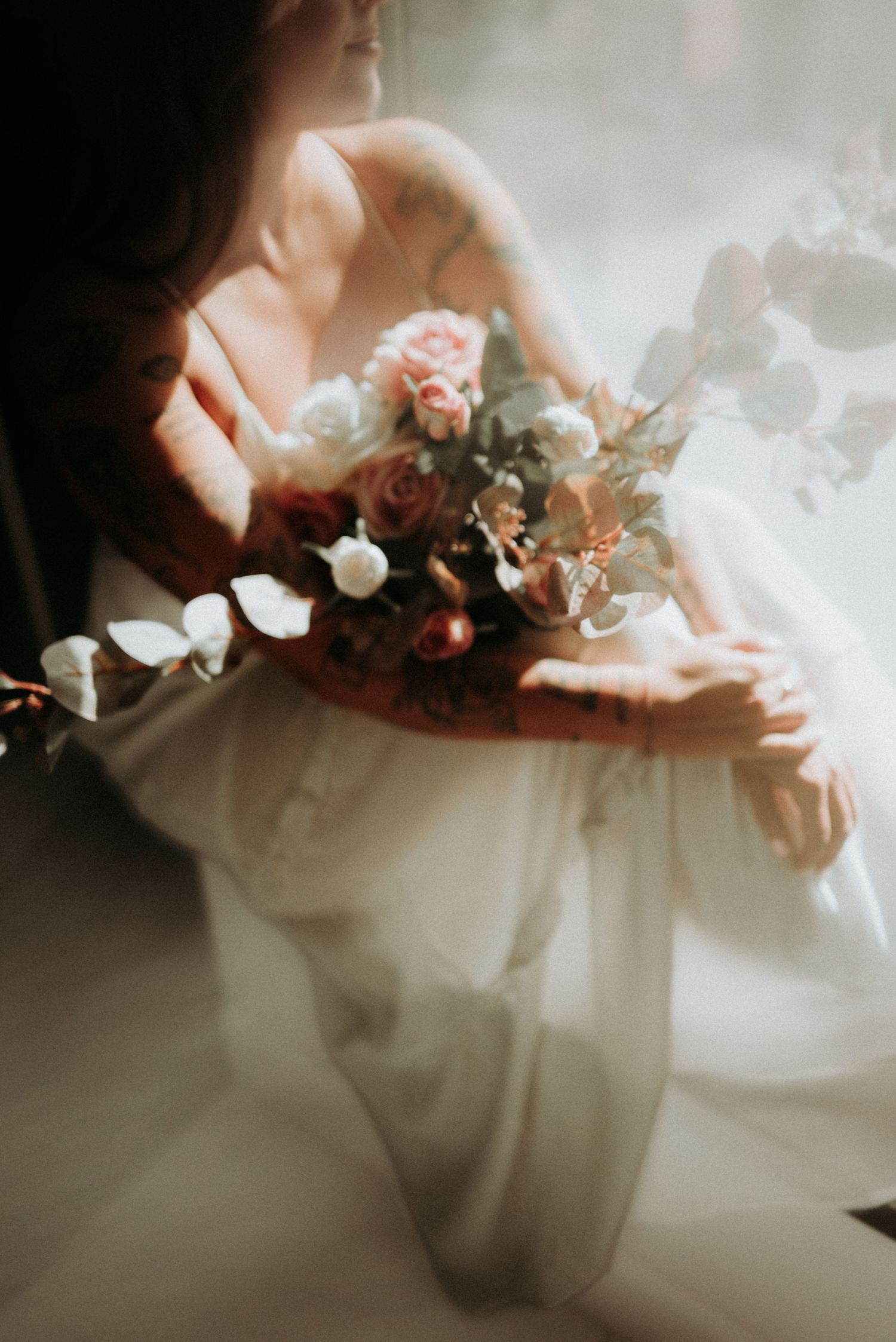 Dreamy ethereal photograph of a bride in white dress holding a romantic bouquet of pink and white flowers in soft light.