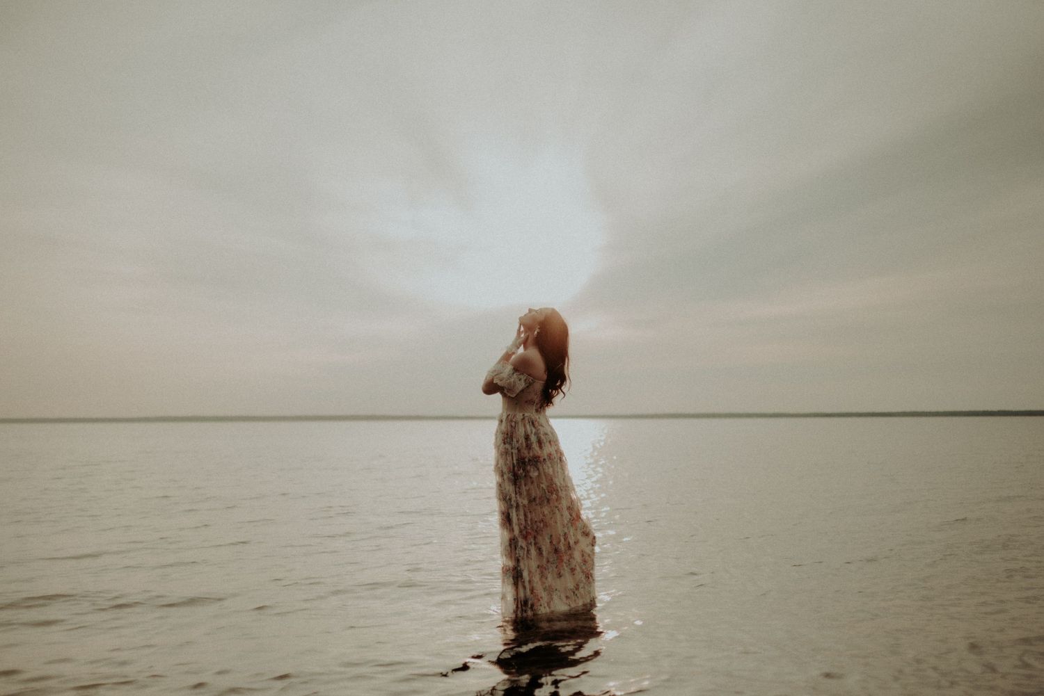 Atmospheric photo of someone in a flowing dress standing in water during golden hour.