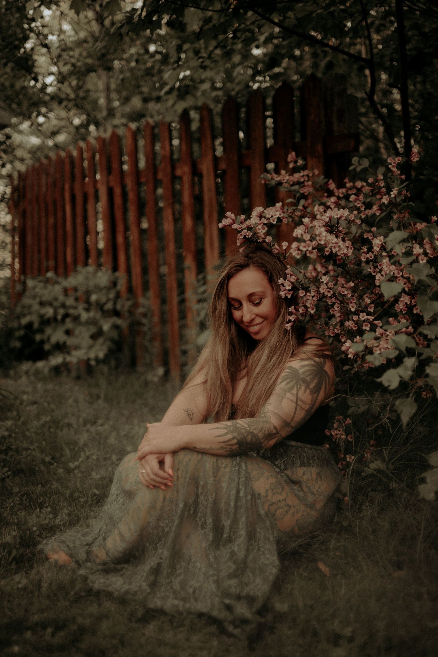 Romantic forest scene with long dress and blooming flowers against rustic fence.