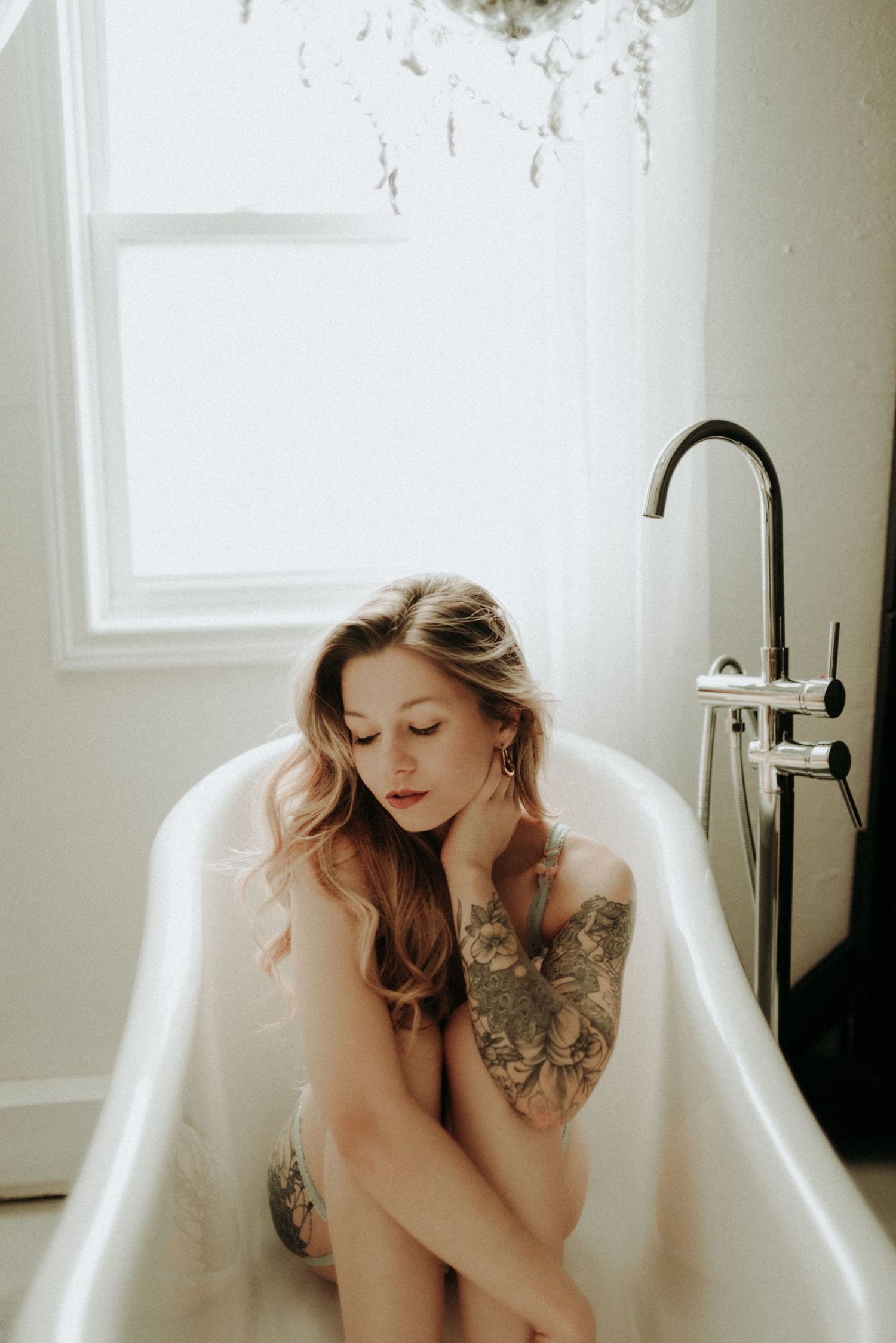 A vintage clawfoot bathtub sits in a bright white room with sunlight streaming through windows.