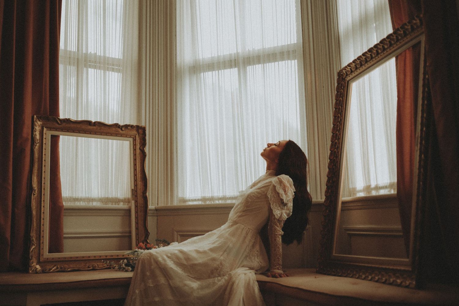 Luxurious vintage interior room with ornate gold mirrors, white curtains, and natural light streaming through windows.