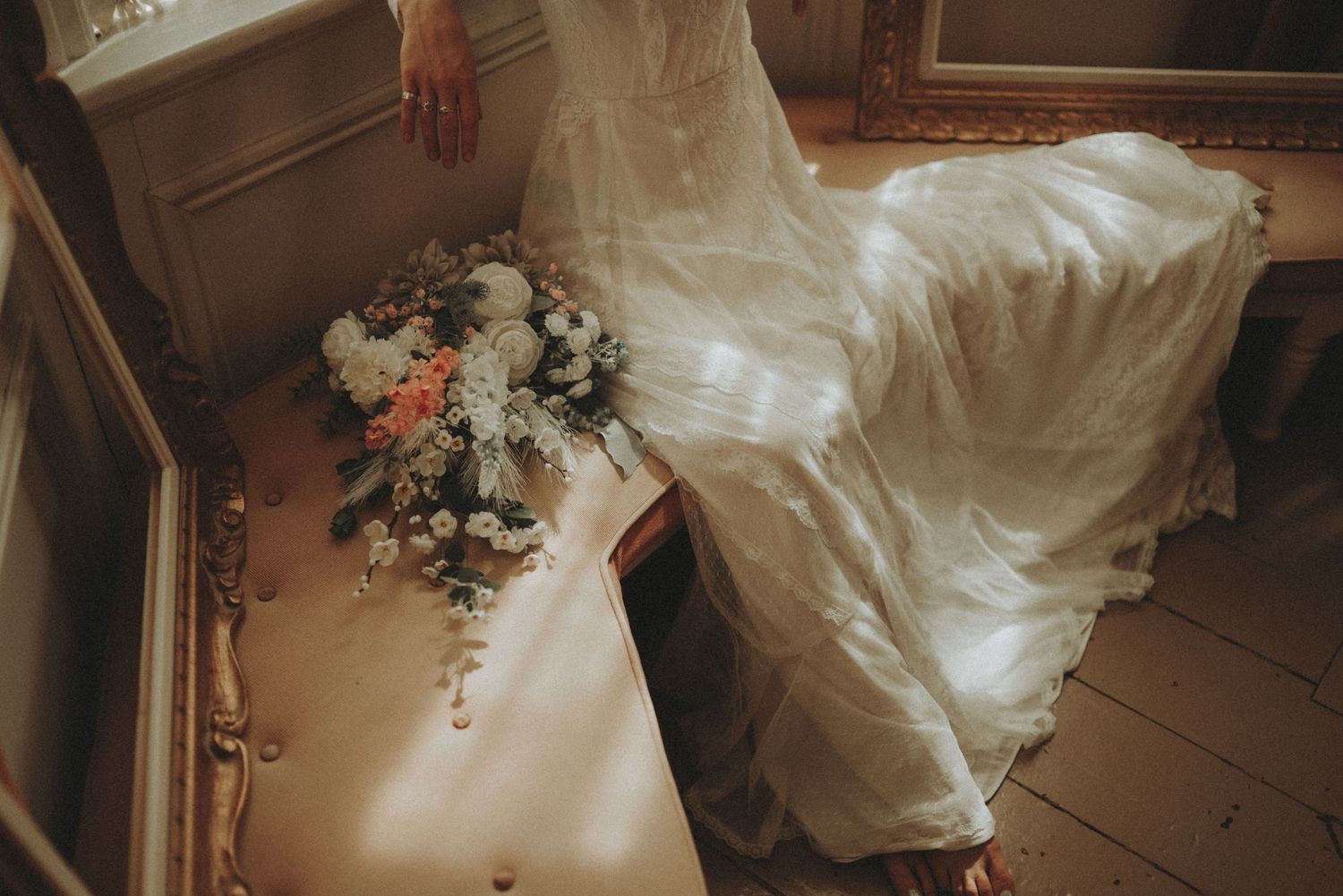 Close-up view of a flowing white wedding dress with delicate lace details trailing on a wooden floor.