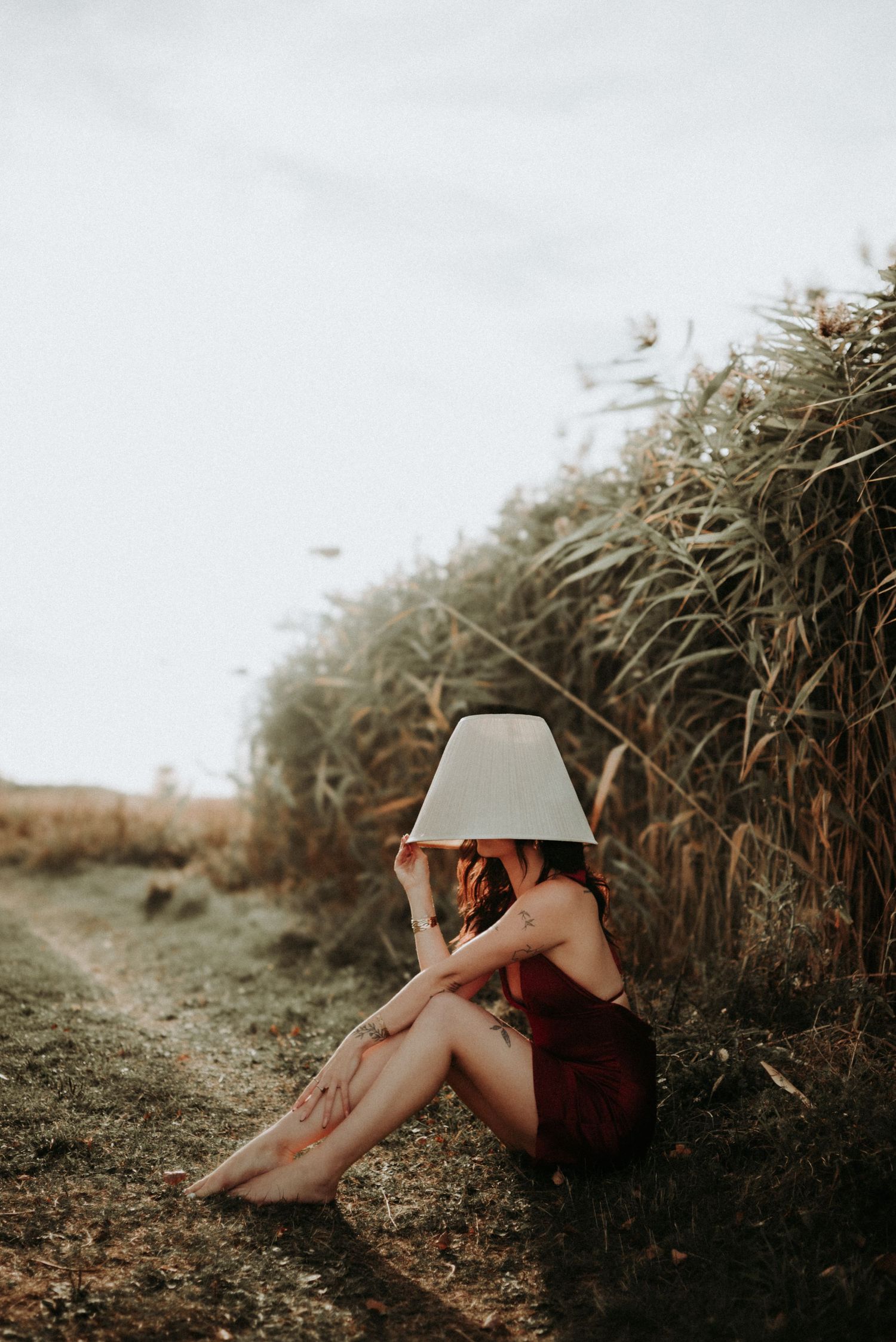 Artistic portrait of a person reclining against tall grass in a moody natural setting at sunset.