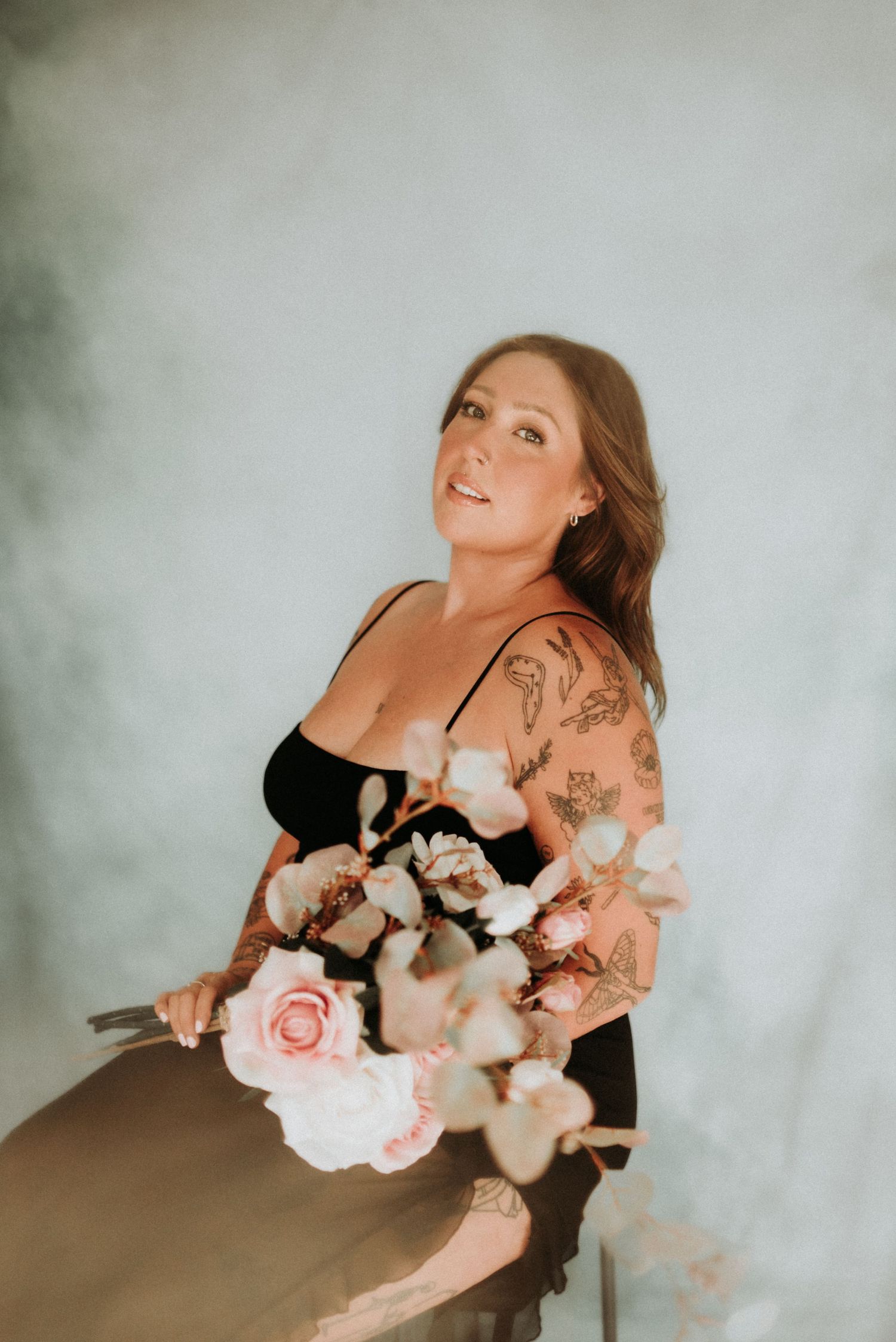 Portrait of someone holding a delicate bouquet of pink roses and cotton stems against a misty background.