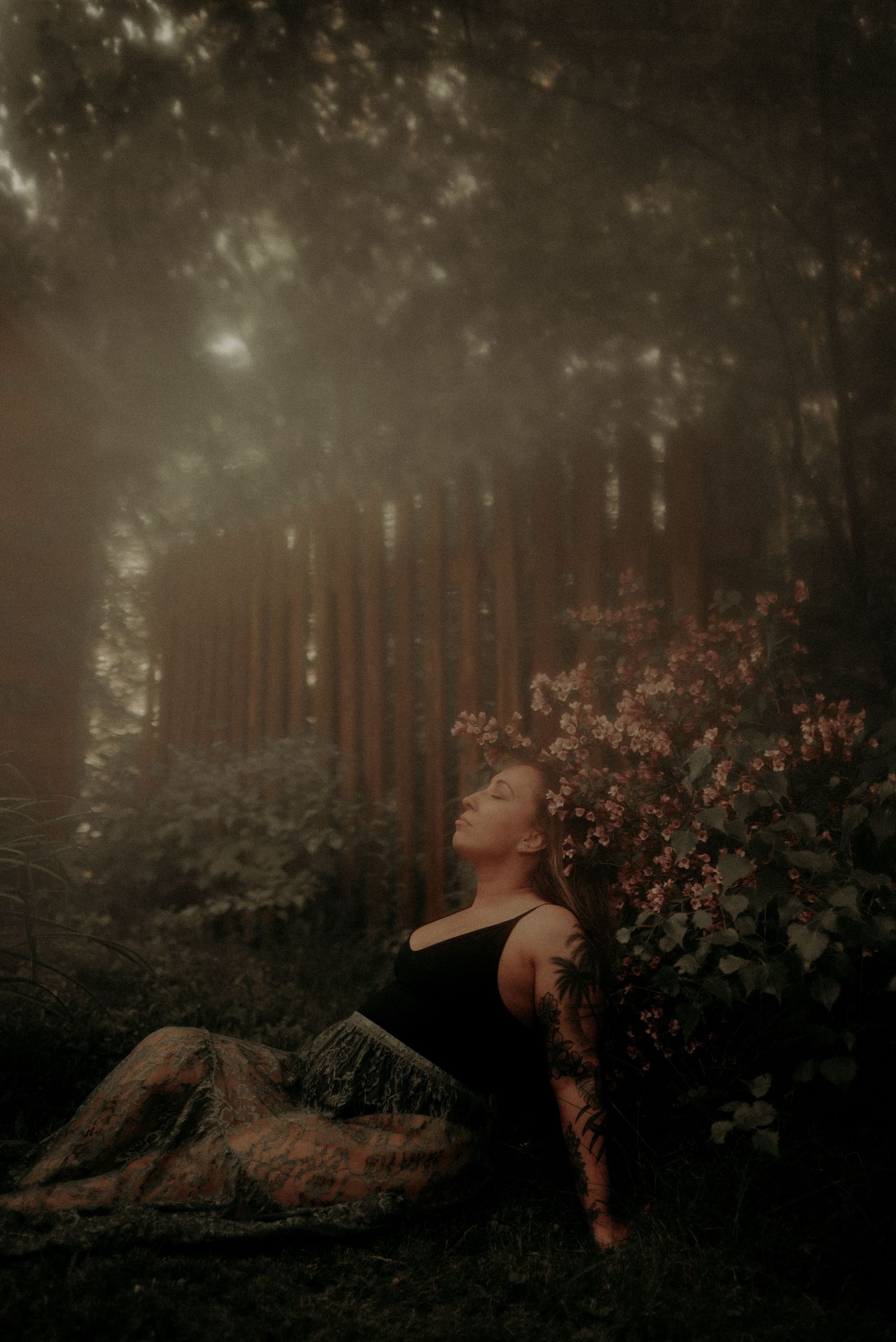 Moody forest portrait with person reclining against rock near blooming flowers in dark atmosphere.