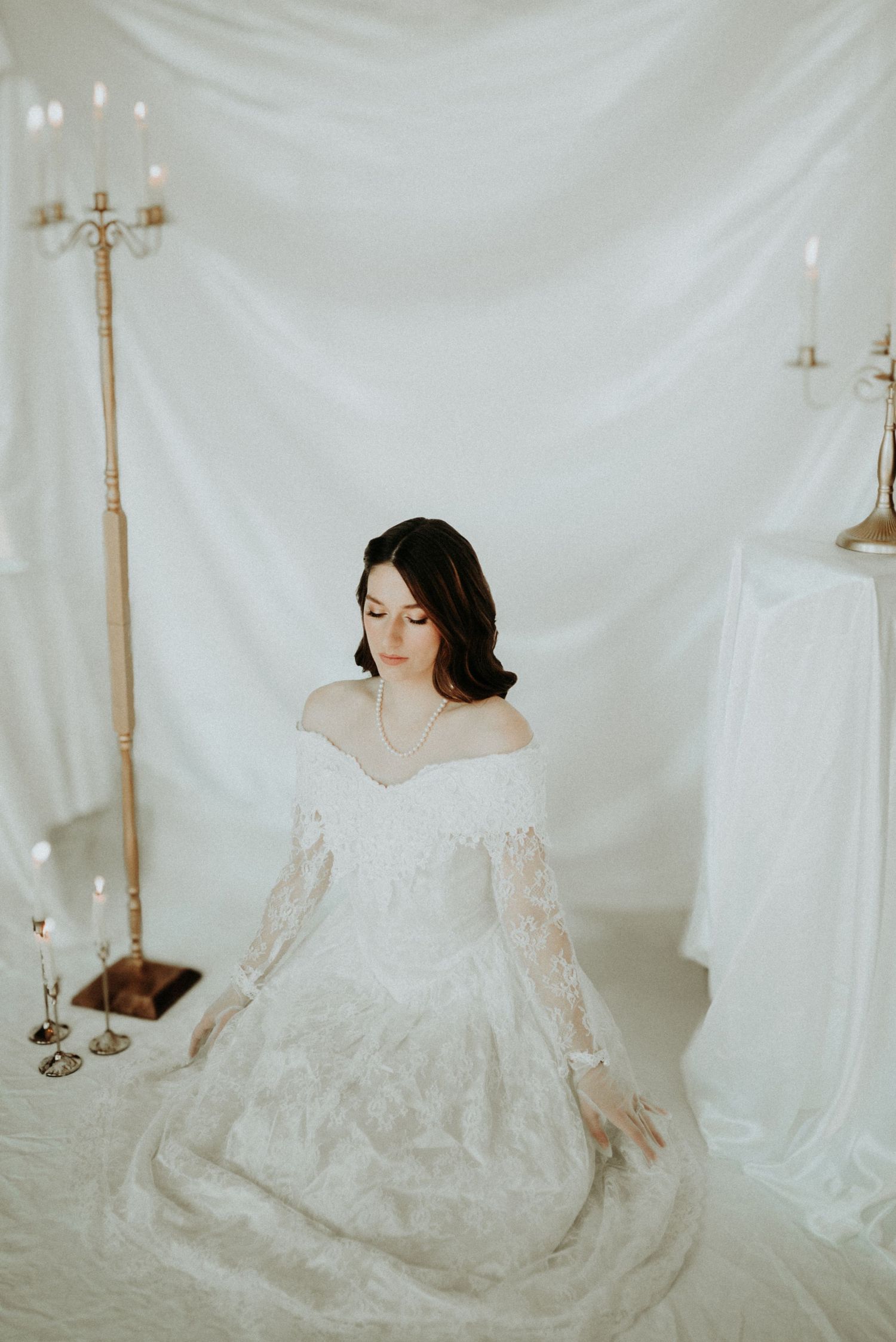 Romantic bridal portrait with flowing white lace gown and antique gold candelabras in studio setting.