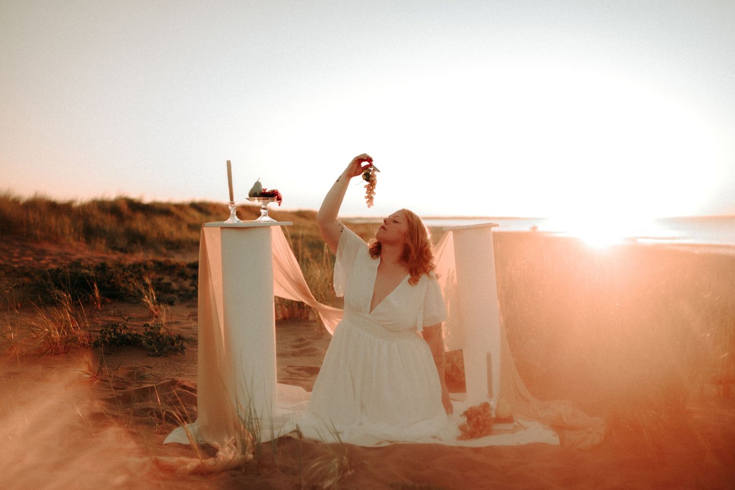 Romantic coastal scene with white dress billowing in the breeze during golden hour photography session.