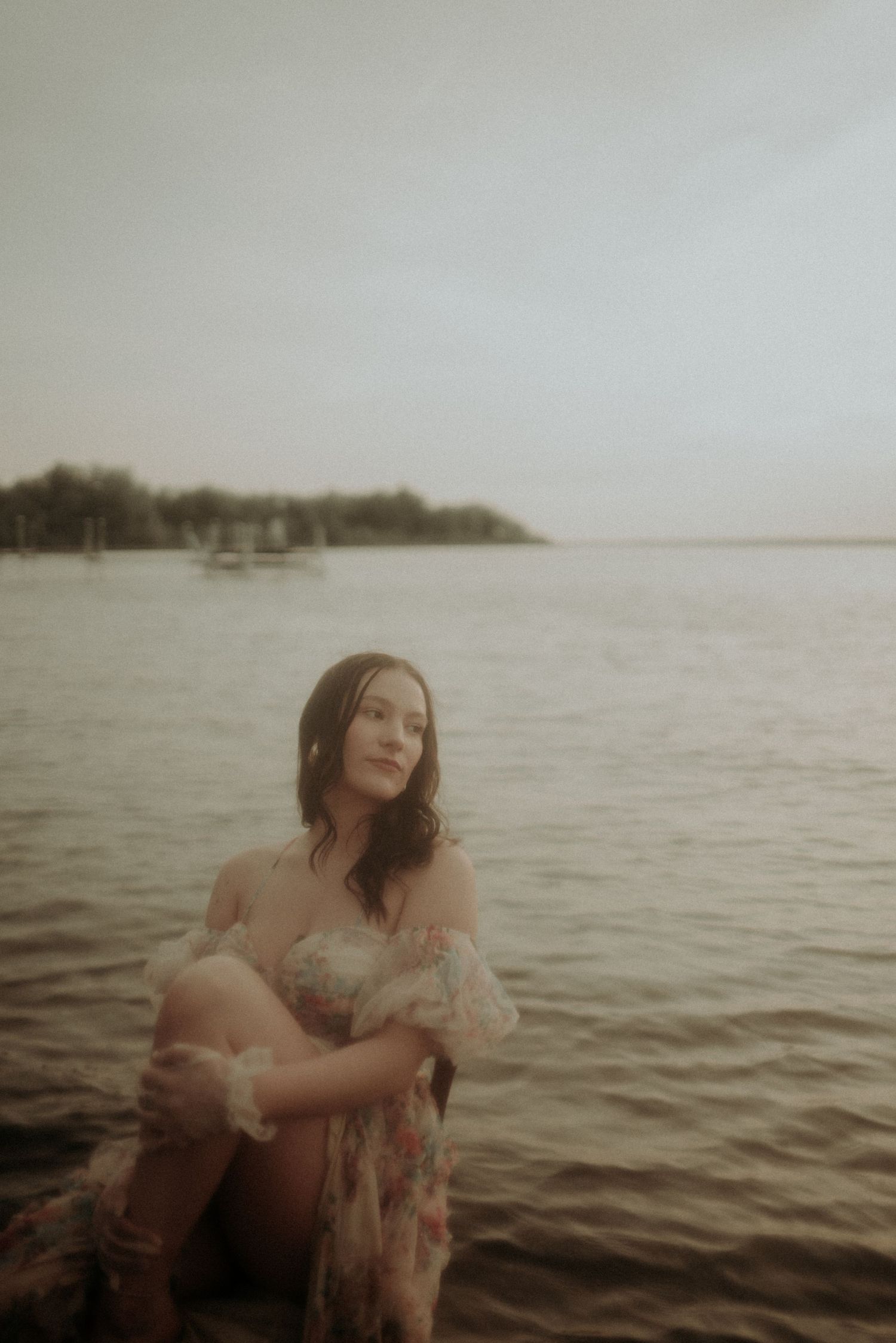 A romantic water photoshoot featuring a flowy dress and moody sepia tones by the shoreline.
