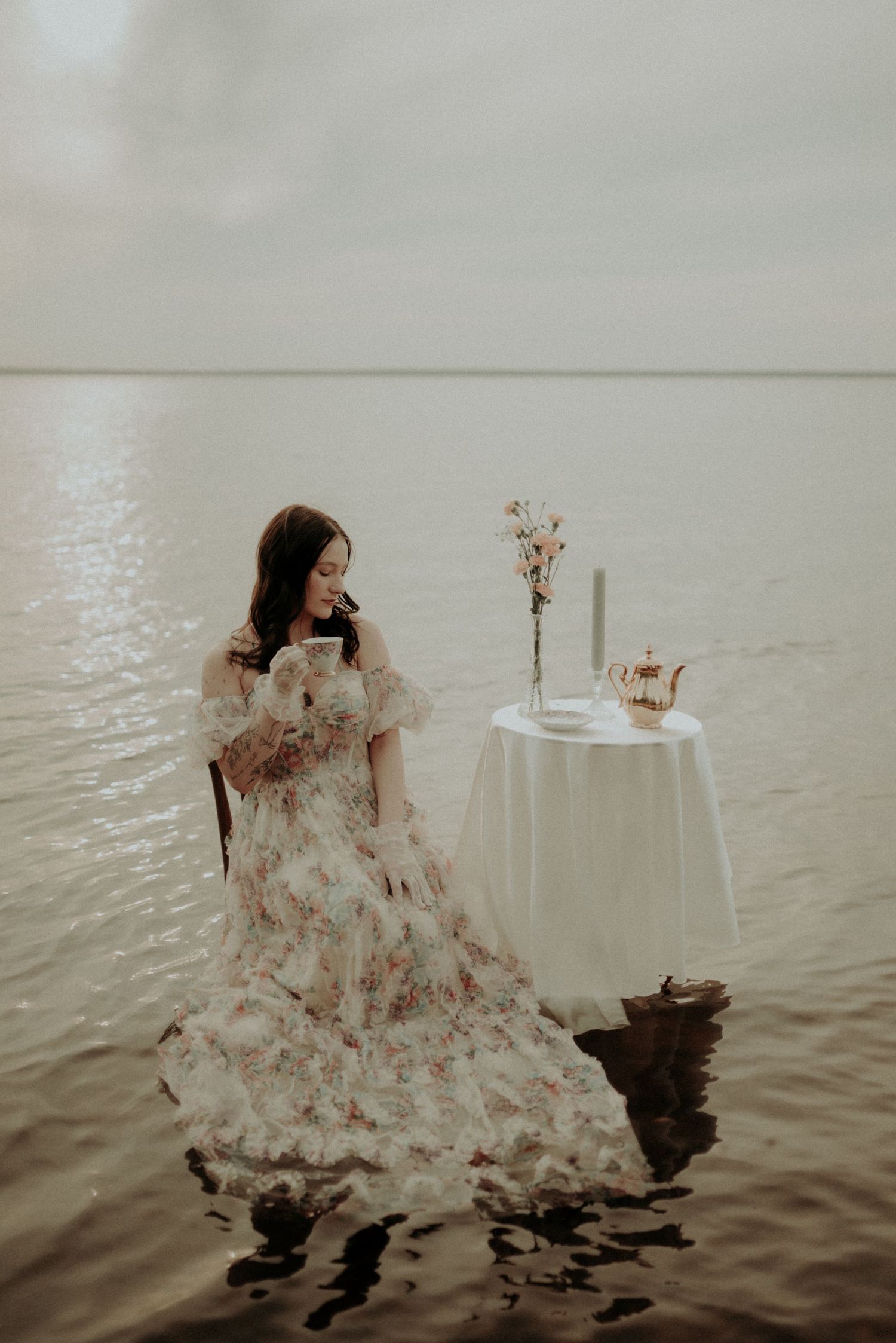 Moody water portrait with flowing dress and white table arrangement in shallow waters.