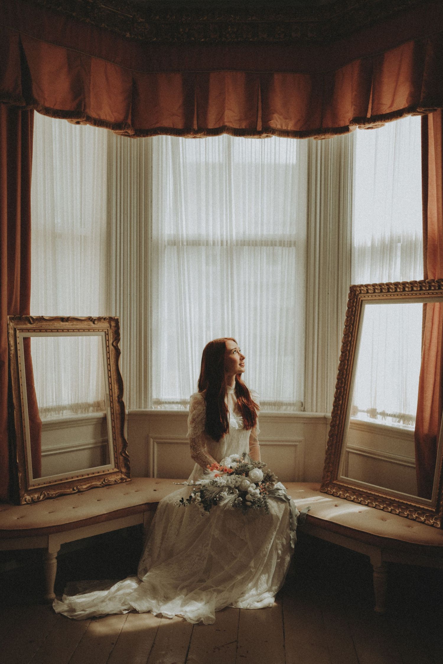 Dramatic indoor portrait in vintage room with ornate mirrors and flowing dress.