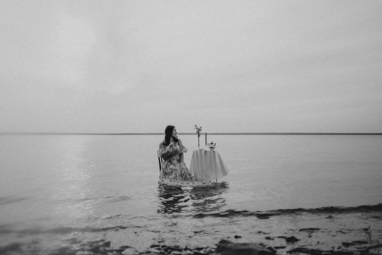 A minimalist photo shoot scene with a table setting and figure in shallow waters.