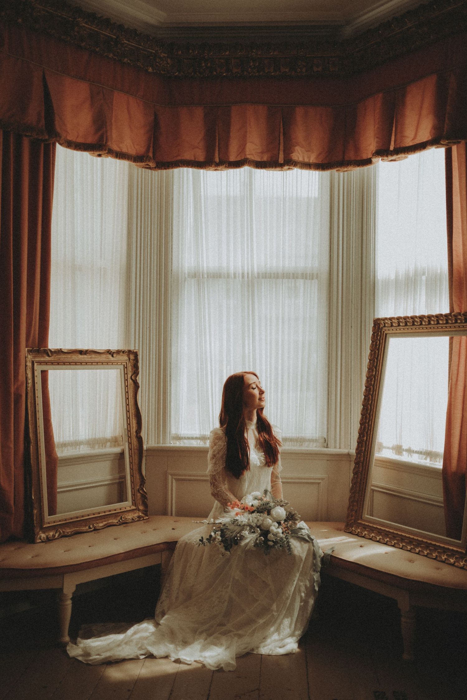 A dreamy bridal portrait in a vintage bay window with flowing white dress and antique gold frames.