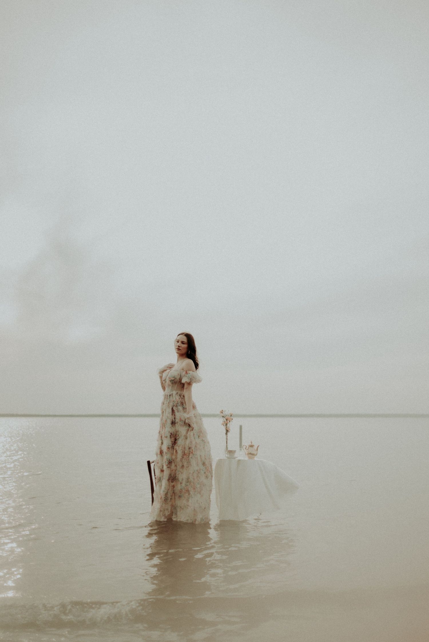 A figure wading through water next to an elegant white table setting in a serene waterscape.