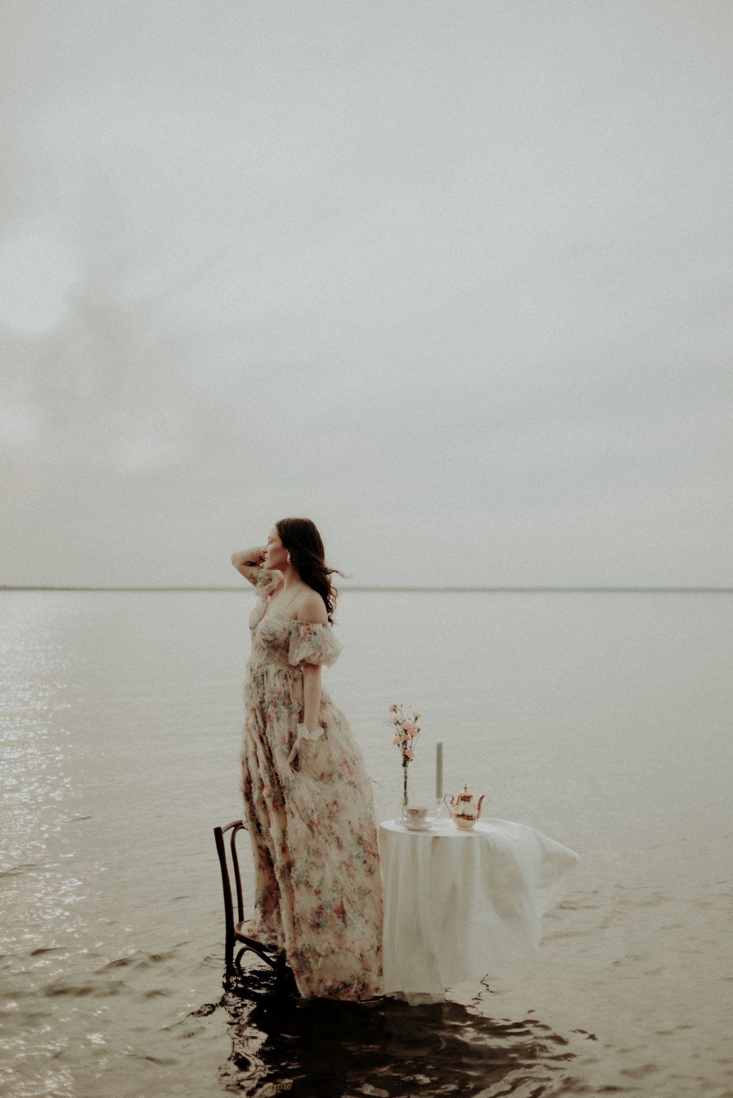 Atmospheric portrait featuring elegant dress and table setting surrounded by calm waters.