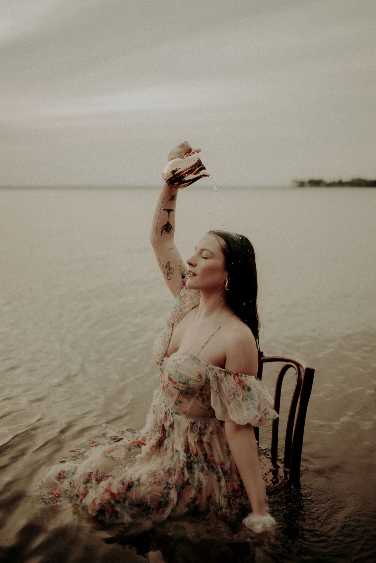 An artistic shot of someone in a vintage floral dress posing with a book in calm waters.