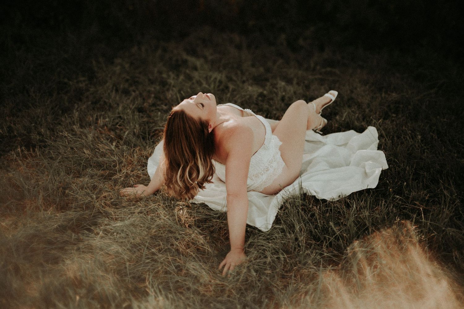 Artistic outdoor boudoir photography with flowing white fabric against dark moody background.