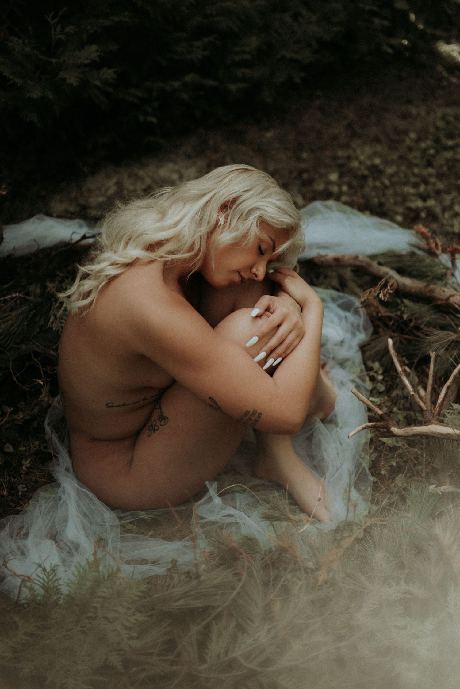 Intimate artistic portrait in nature with gentle lighting and flowing fabric elements.