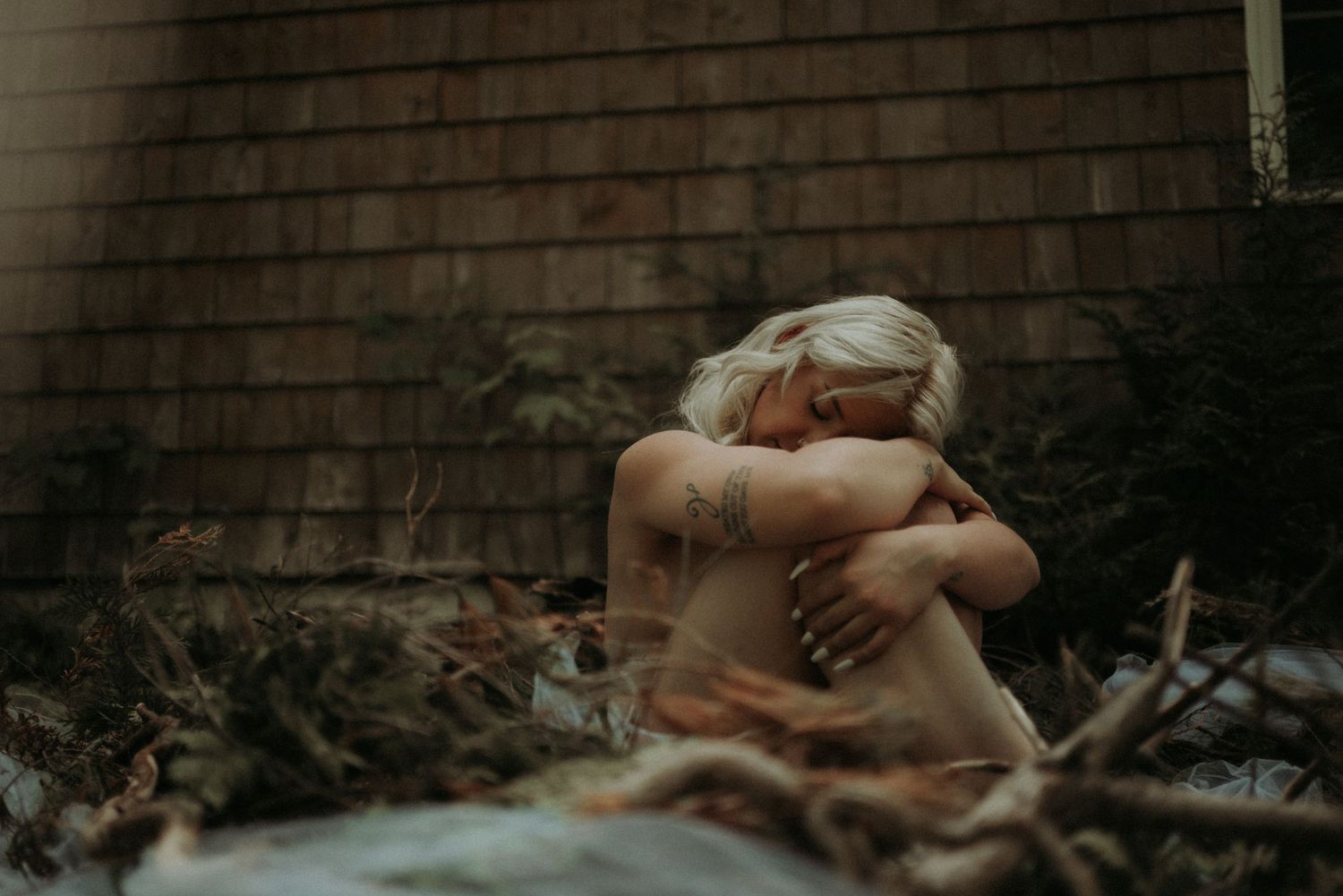 Figure resting against rustic wooden wall in natural outdoor setting.