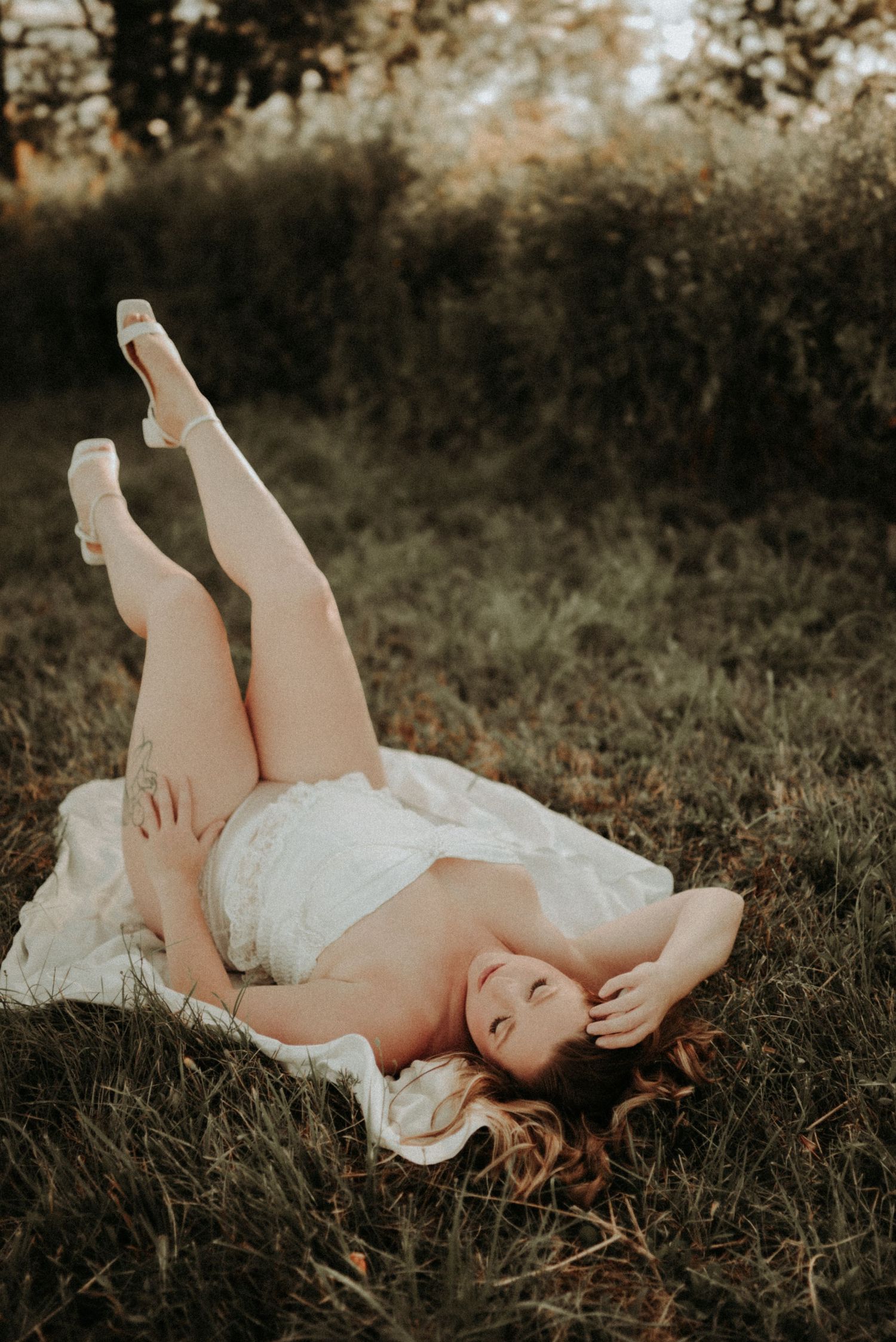 A person in a white dress lying on grass in a dreamy outdoor setting with moody lighting.