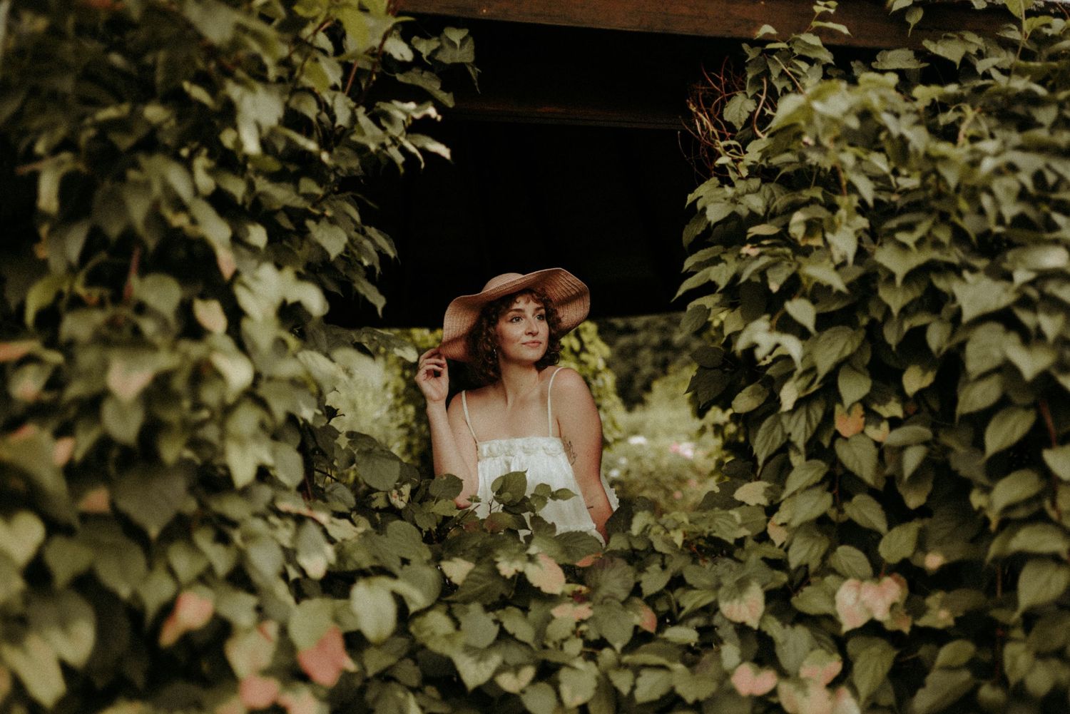 A couple in wedding attire poses together in a lush garden setting with green foliage surrounding them.