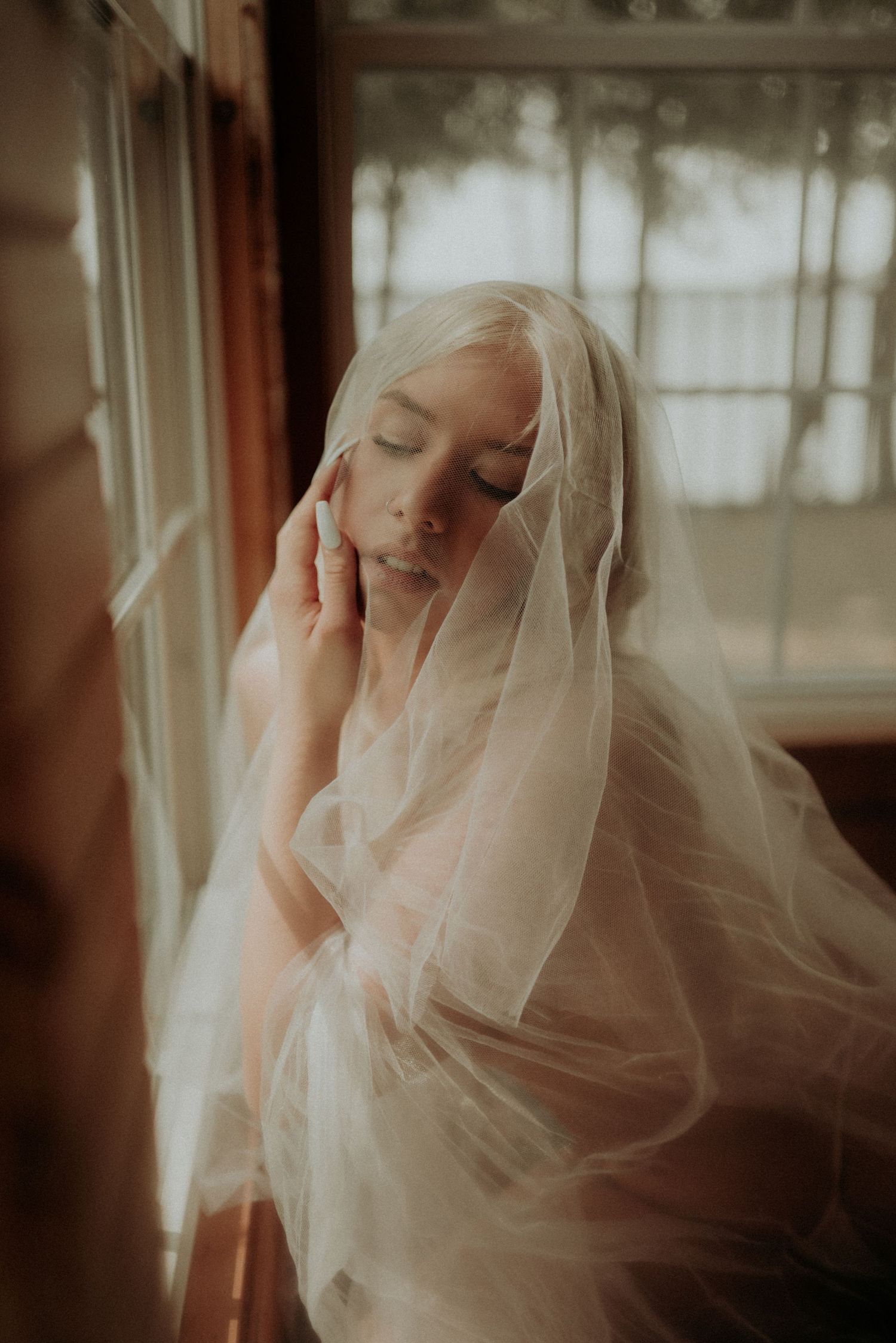 Dreamy portrait series with sheer veil creating romantic atmosphere by window.