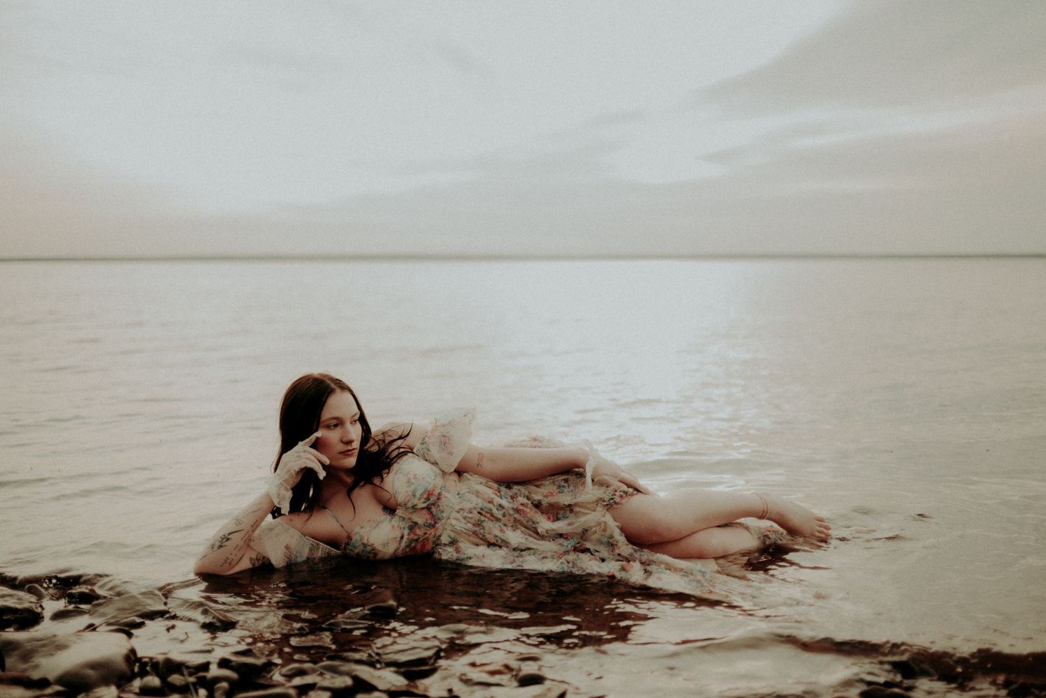 Ethereal portrait of a person lying in shallow water wearing a romantic vintage dress.