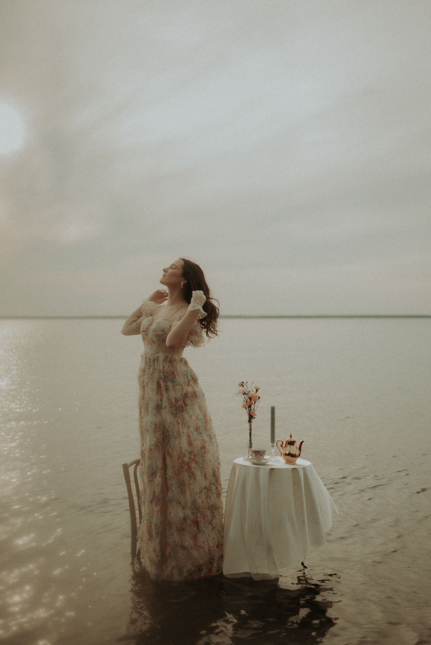 Dreamy portrait with someone in a floral dress standing beside an elegant table setting in water.