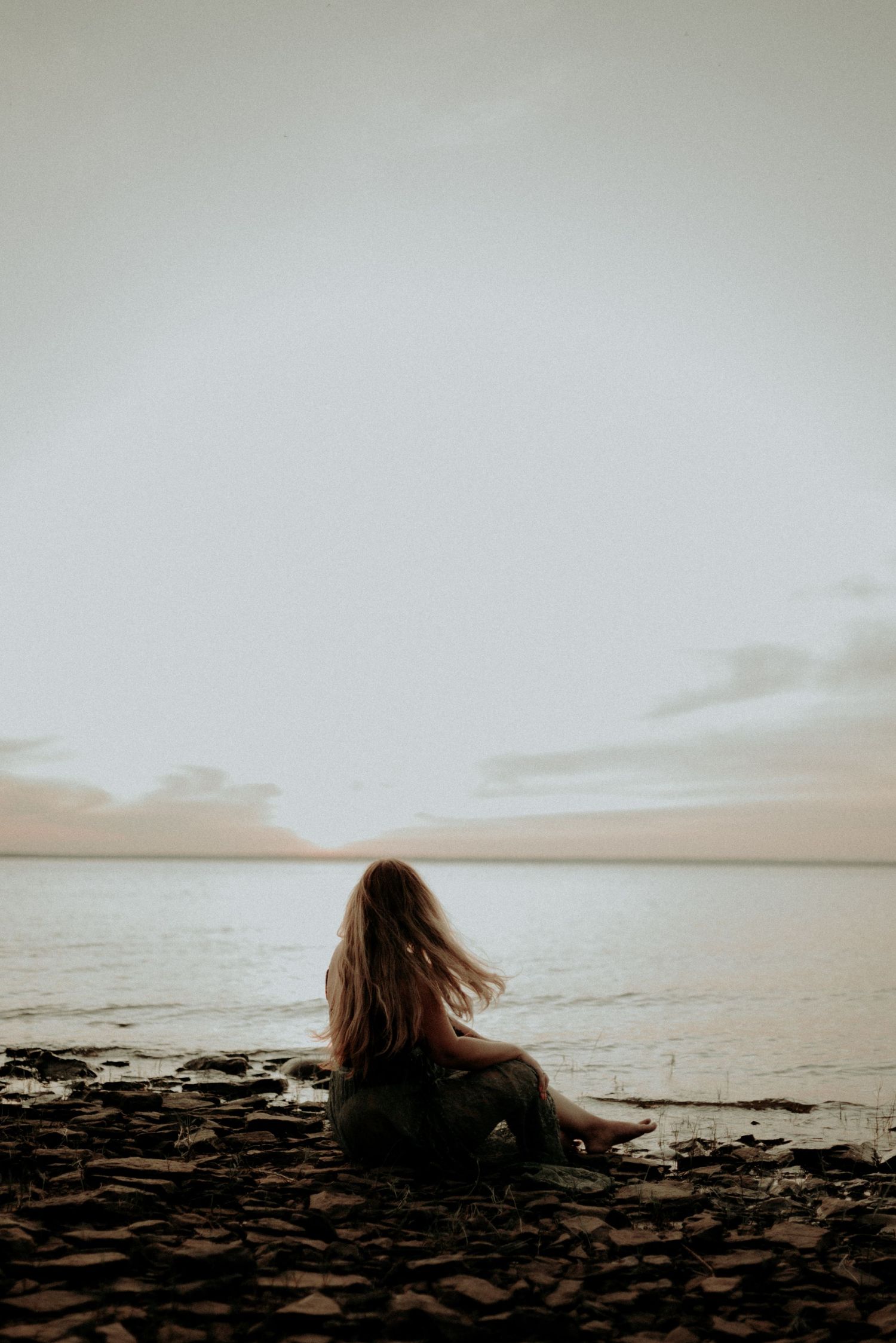 Dreamy silhouette sitting on rocky beach during sunset.