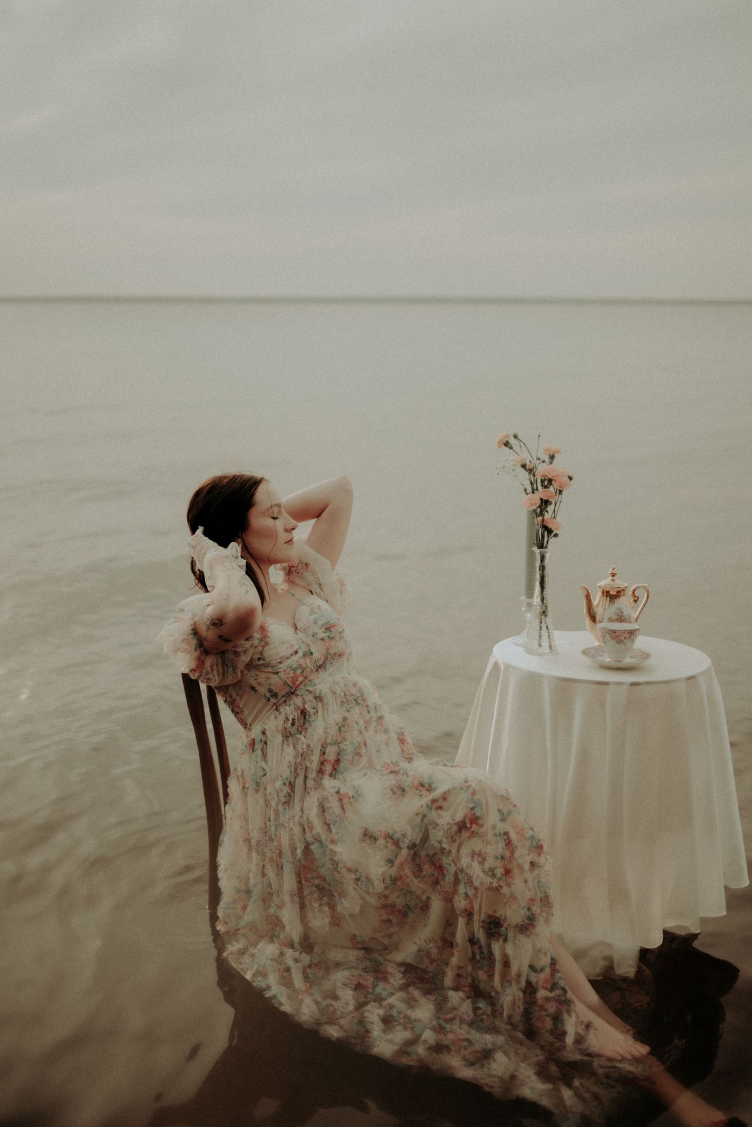 A dreamy photoshoot in water with a table setting and flowing floral dress creating an ethereal atmosphere.