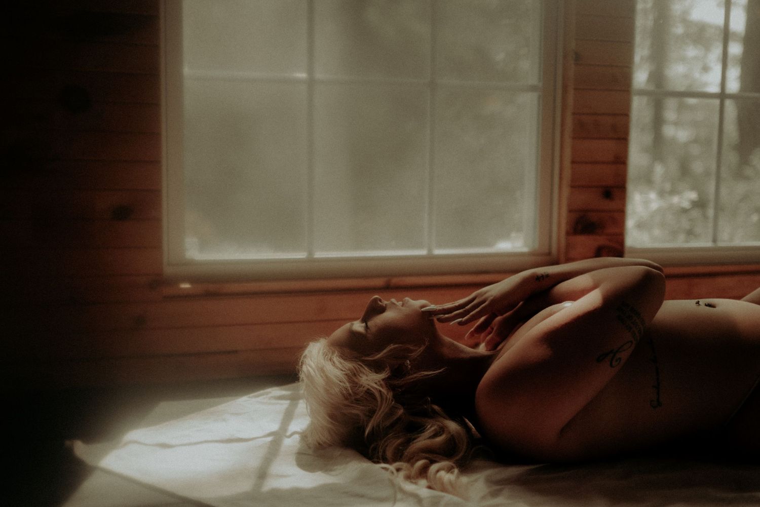 Artistic indoor portrait with moody lighting and rustic wooden window frames.