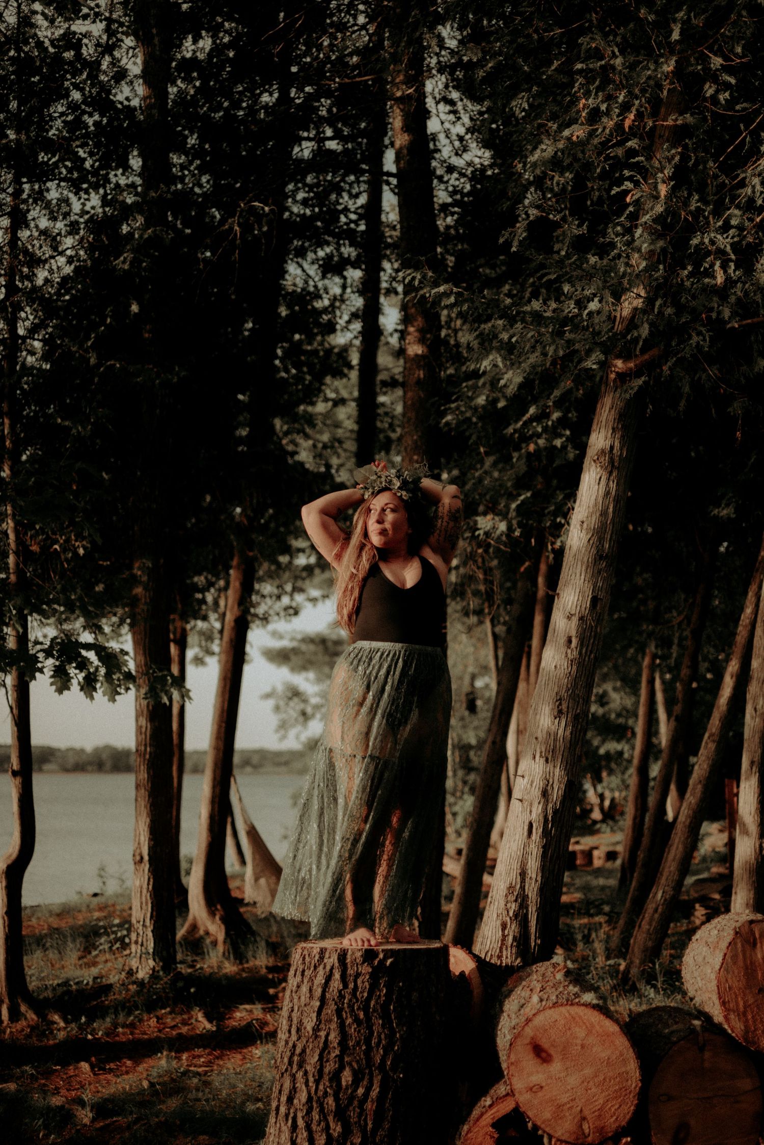 Figure standing on tree stump by lakeside in warm sunset lighting.