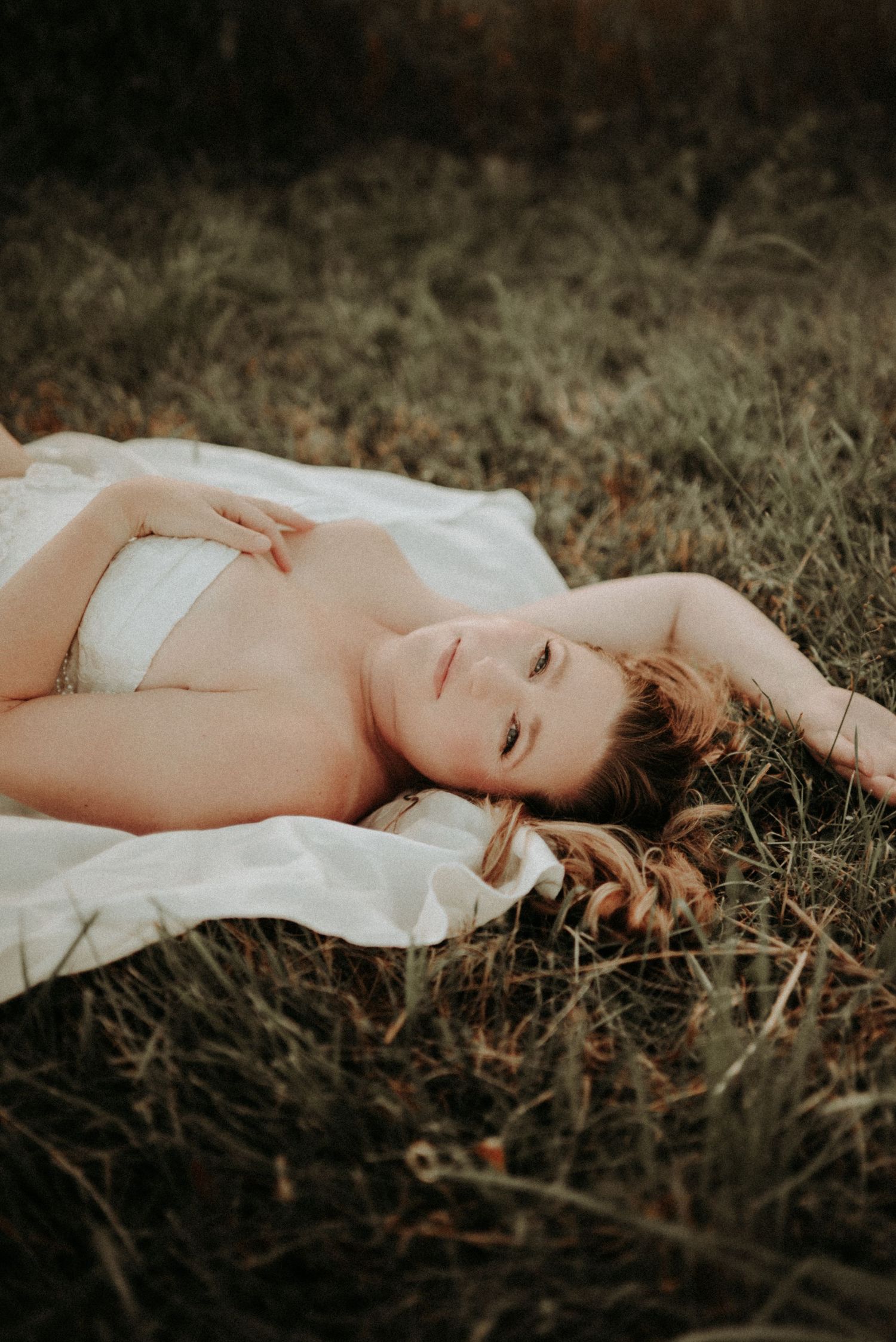 Dramatic portrait showing someone reclining on autumn grass in delicate white fabric.
