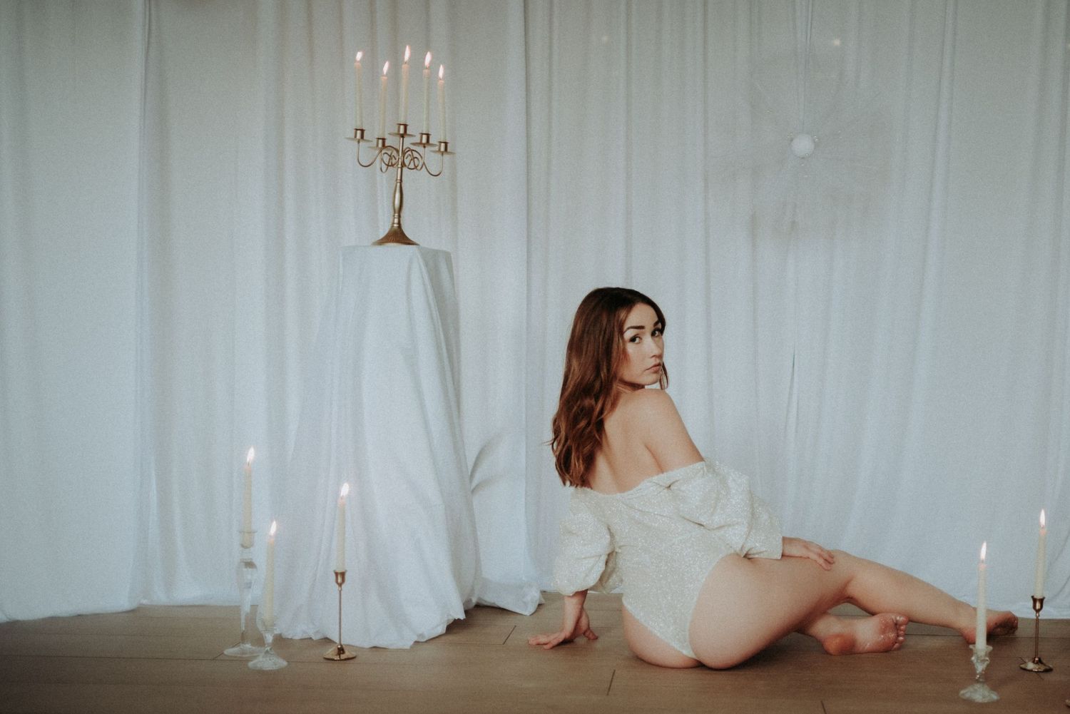 Elegant boudoir photography set featuring white drapes, candles and dramatic lighting.