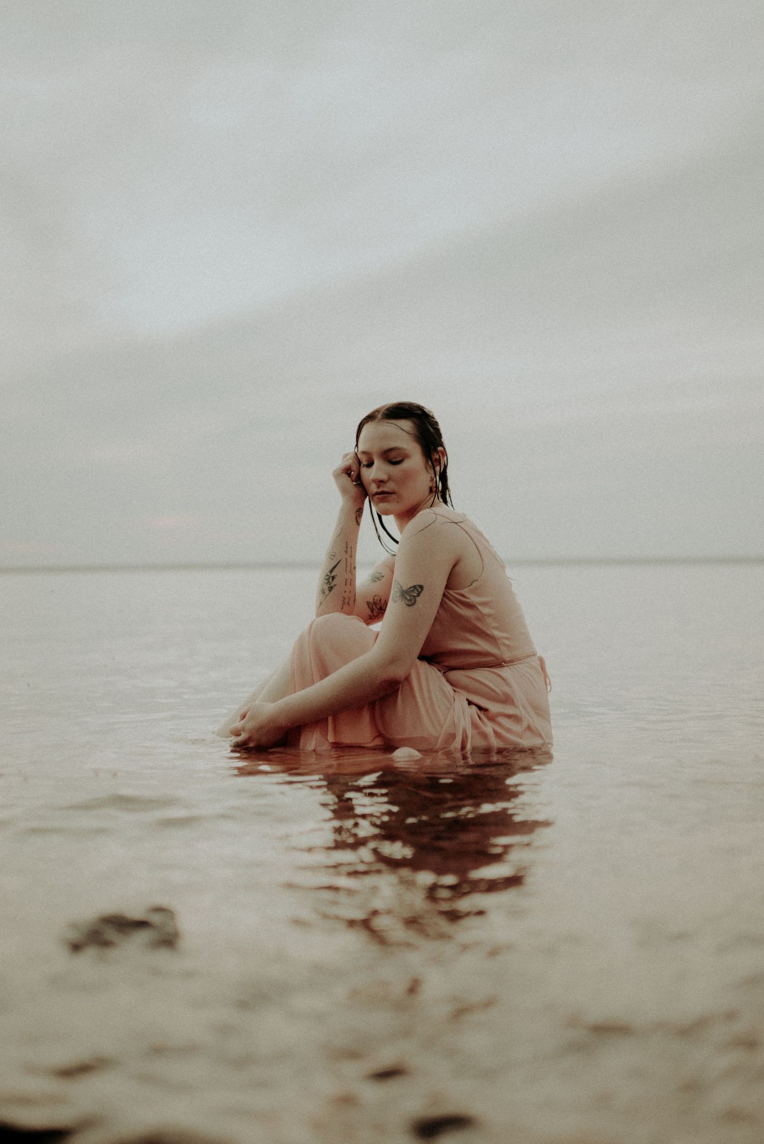 A melancholic portrait of someone sitting in calm waters during sunset.