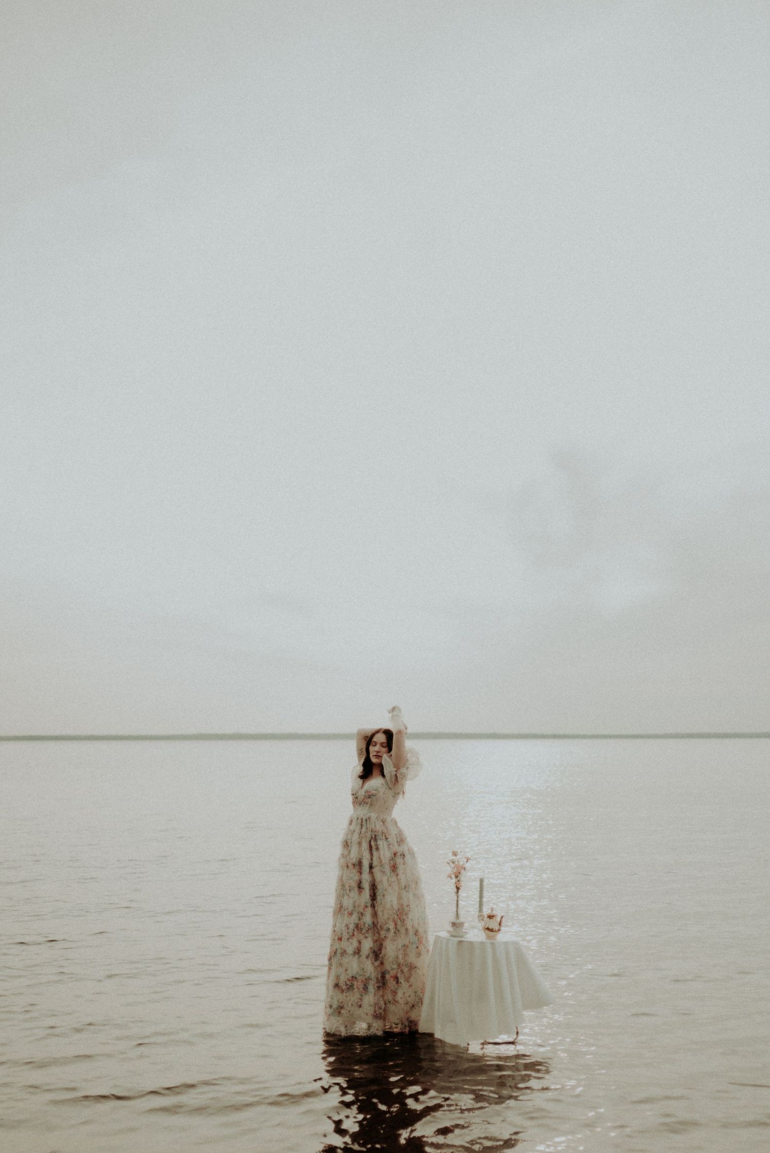 Long floral dress silhouetted against foggy waterscape with table setting.