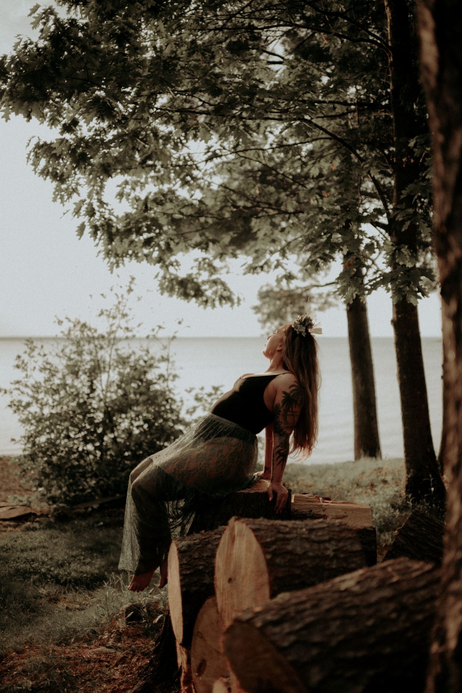 Dramatic forest portrait with figure leaning back on fallen logs near water.