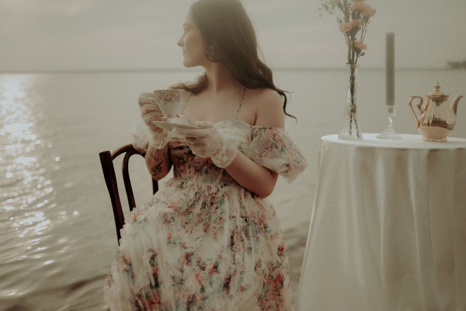 Ethereal waterside photoshoot featuring a table setting and flowing dress against calm waters.