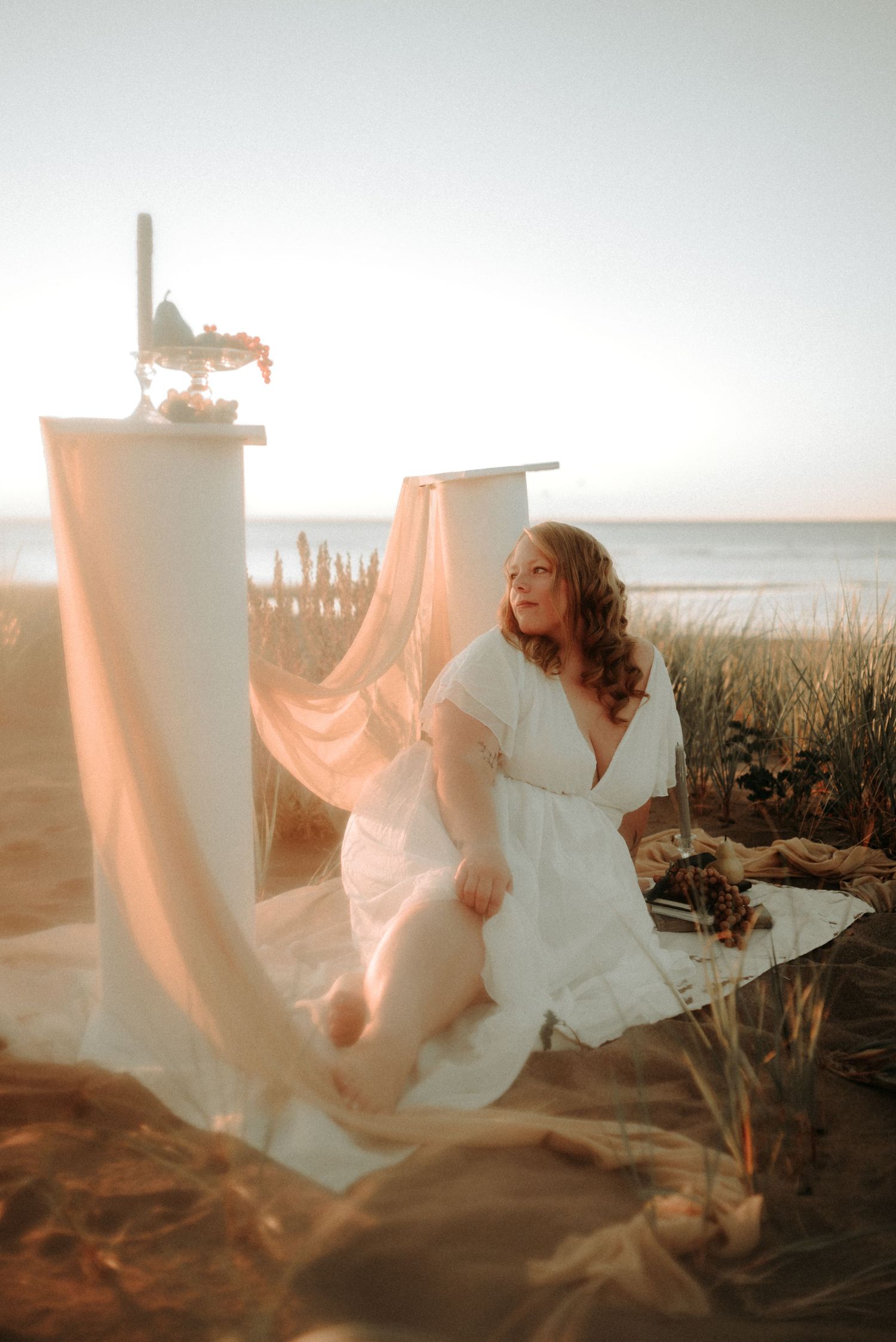 Ethereal figure in white dress dances through coastal grass at sunset creating dreamy motion blur effect.