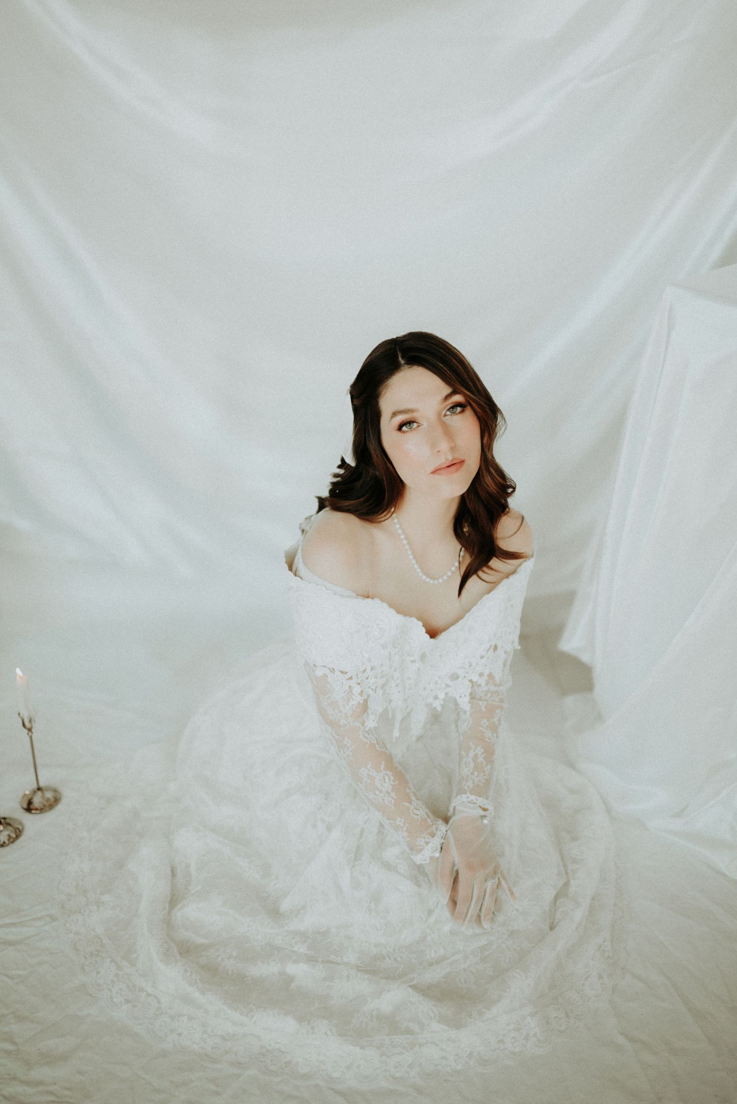 Ethereal bridal portrait featuring a delicate off-shoulder lace gown against a soft white backdrop.