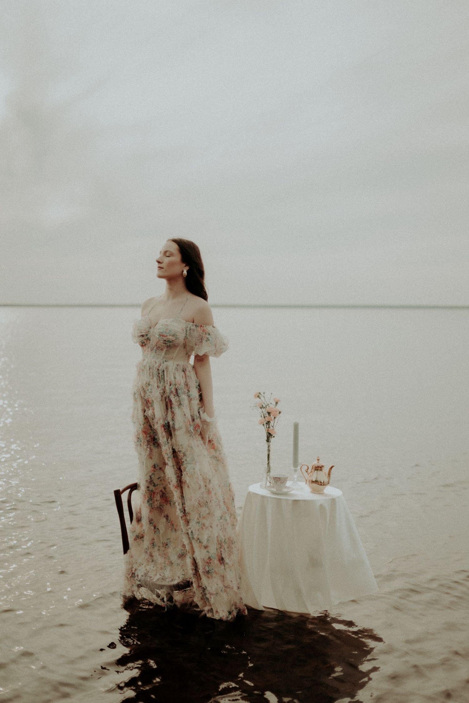 Dreamy photoshoot featuring a flowing floral gown and elegant table setting in tranquil waters at dusk.
