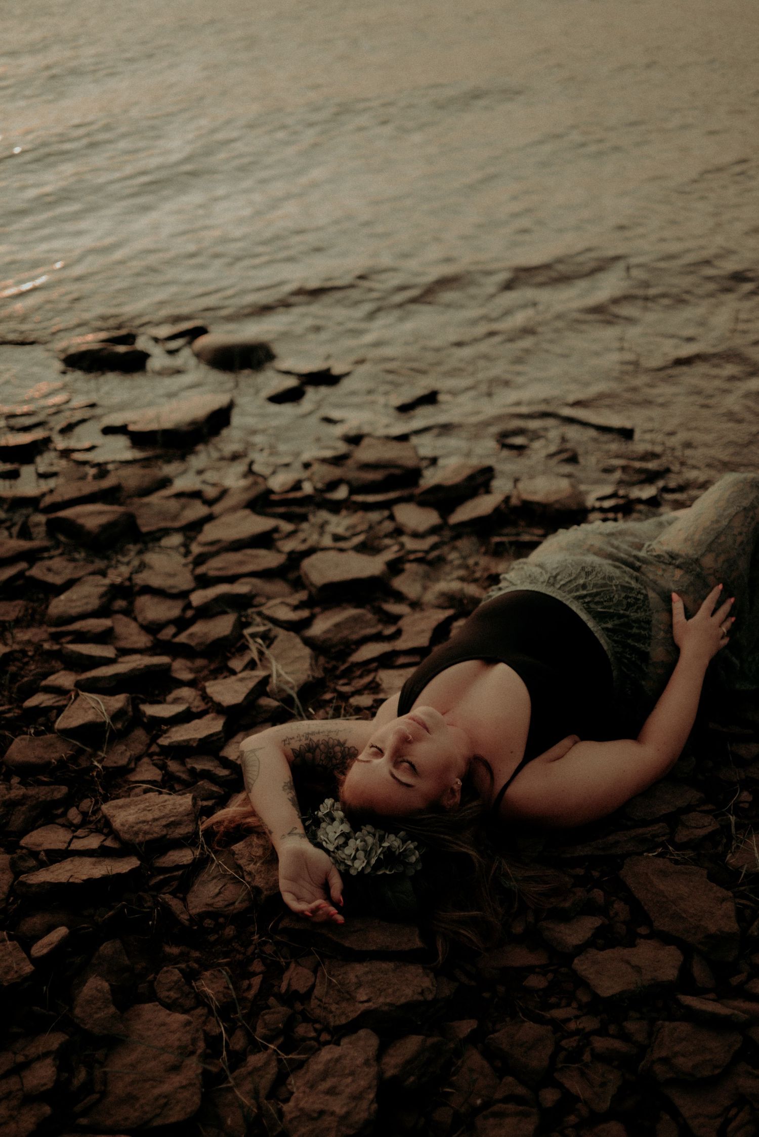 Artistic portrait on rocky beach during golden hour with dramatic lighting.