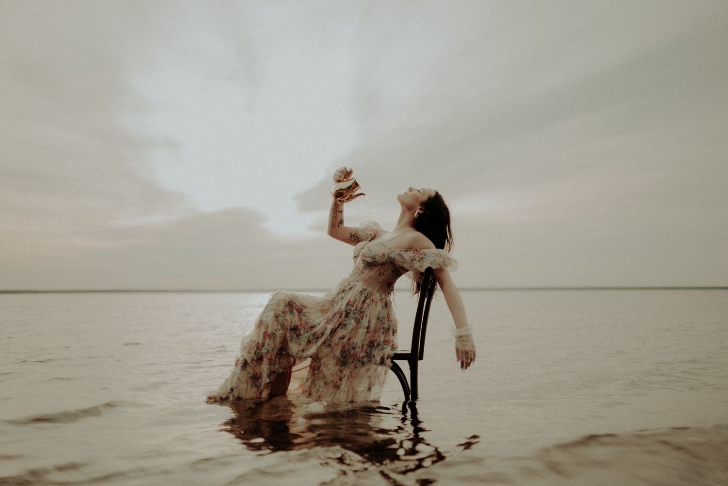 Dramatic water portrait featuring a vintage dress and wooden chair in a misty lake setting.