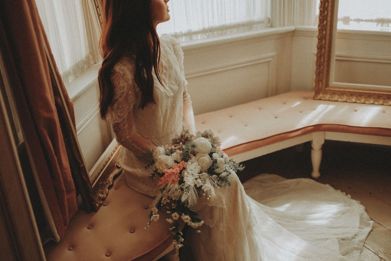 Moody wedding photography featuring ornate window frames and dramatic dress silhouette in natural light.