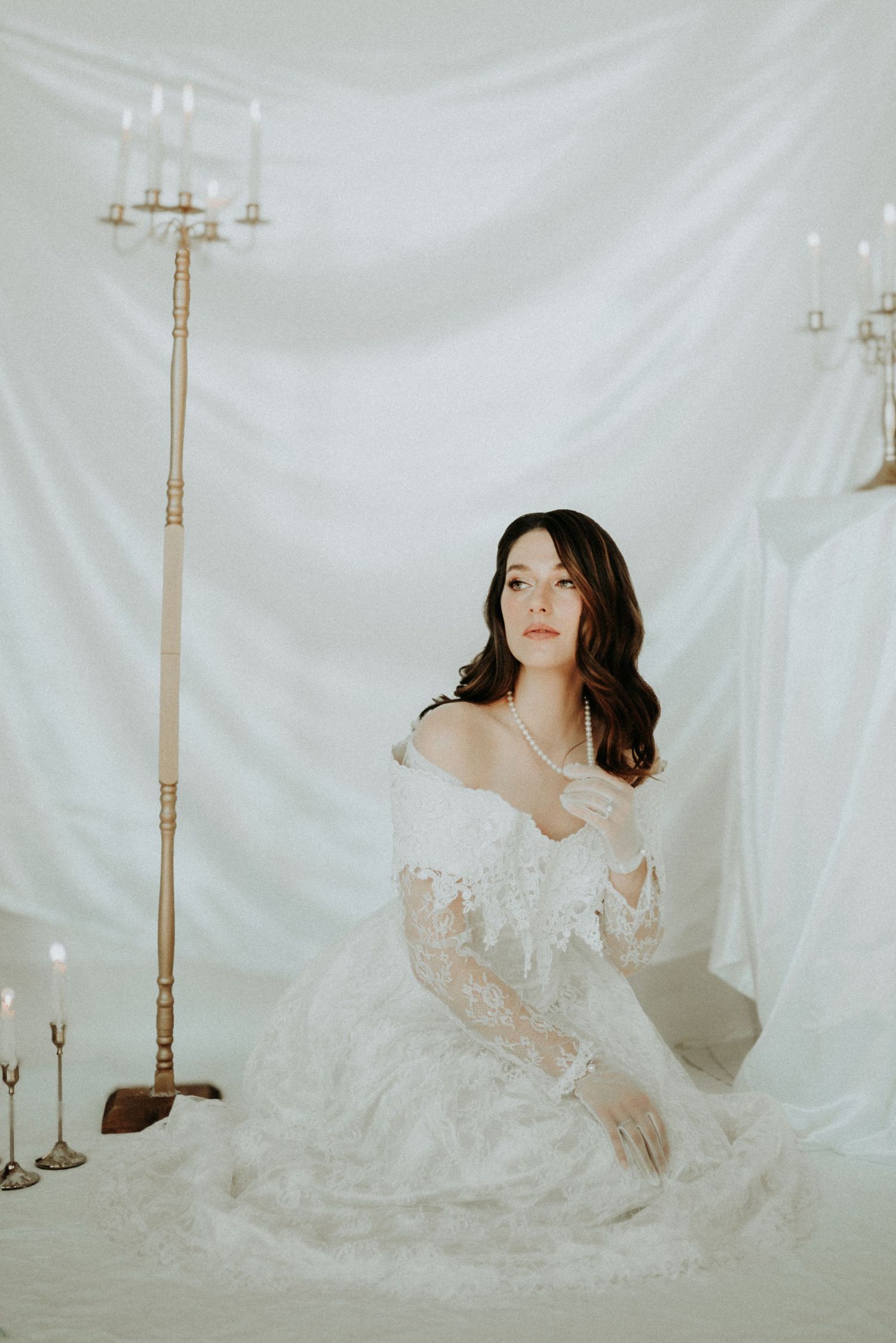 Ethereal portrait session featuring delicate lace dress against white backdrop with vintage candelabras.