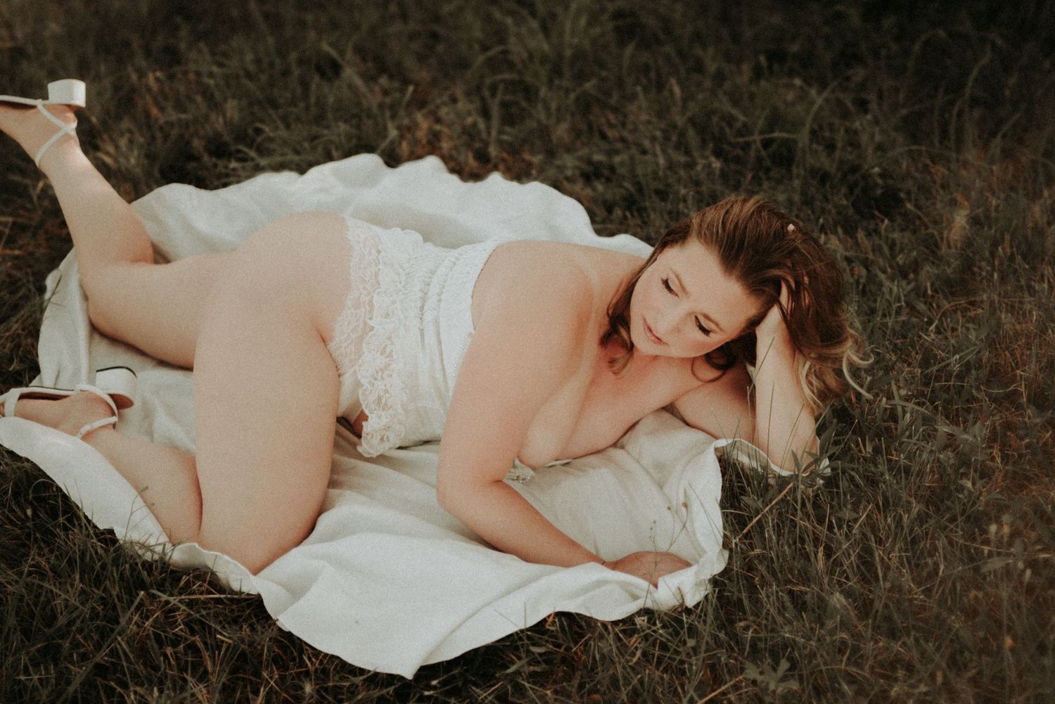 Woman in white dress lying on brown grass in artistic outdoor photo series.