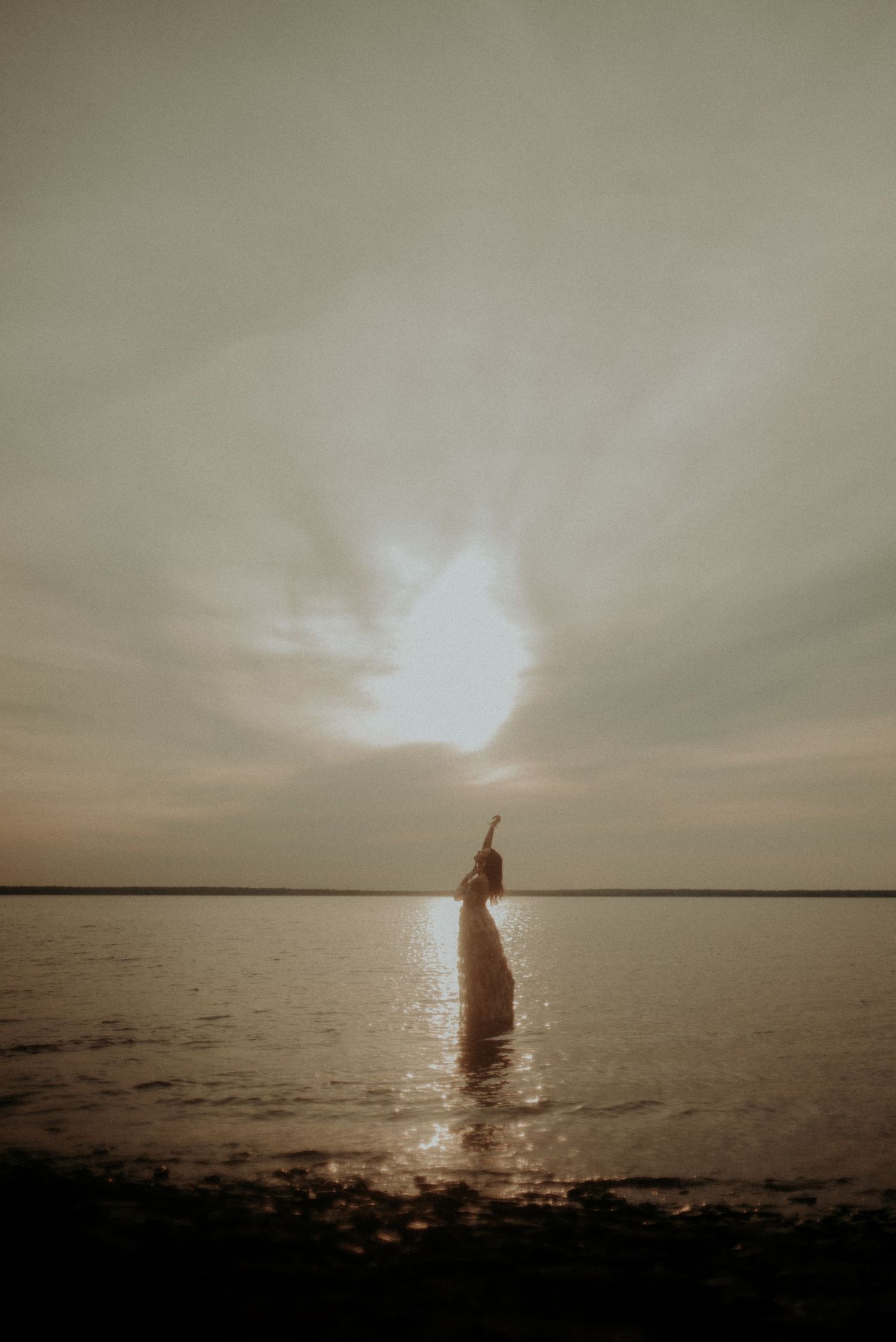 Ethereal silhouette against setting sun stands in shallow water creating dramatic backlit scene.