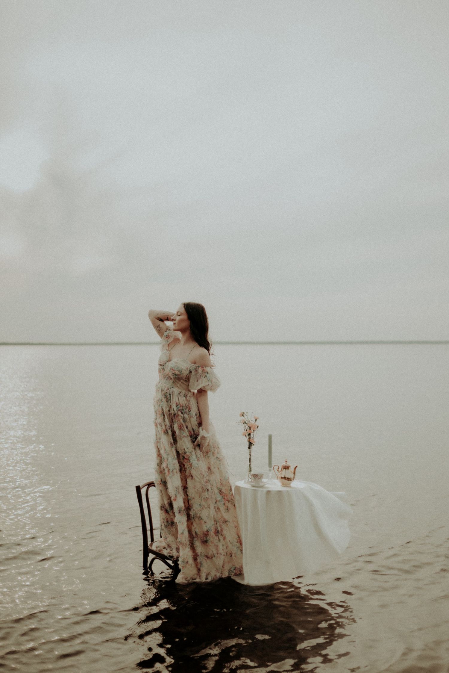 Ethereal waterside portrait with vintage dress and intimate table setting.