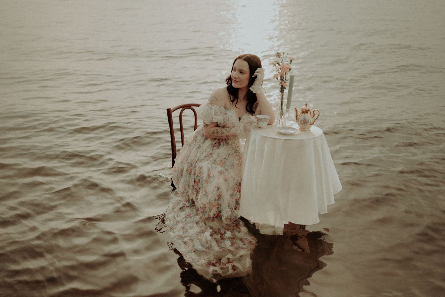 Romantic waterside scene with vintage table settings and flowing dress creating a dreamy atmosphere.