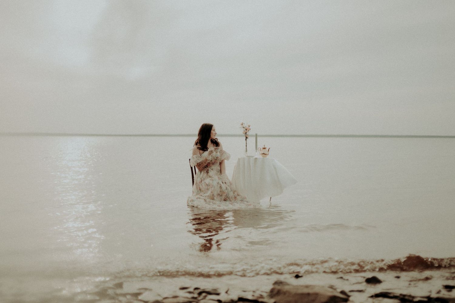 An artistic water photoshoot featuring a white table setting and flowing dress in muted tones.
